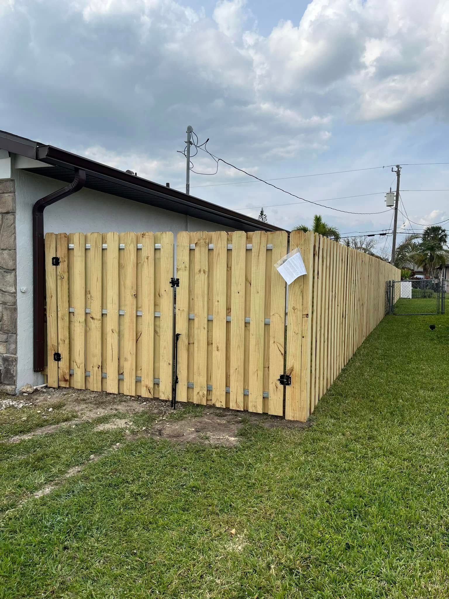Wooden fence surrounding a house with a green lawn. Cloudy sky overhead.