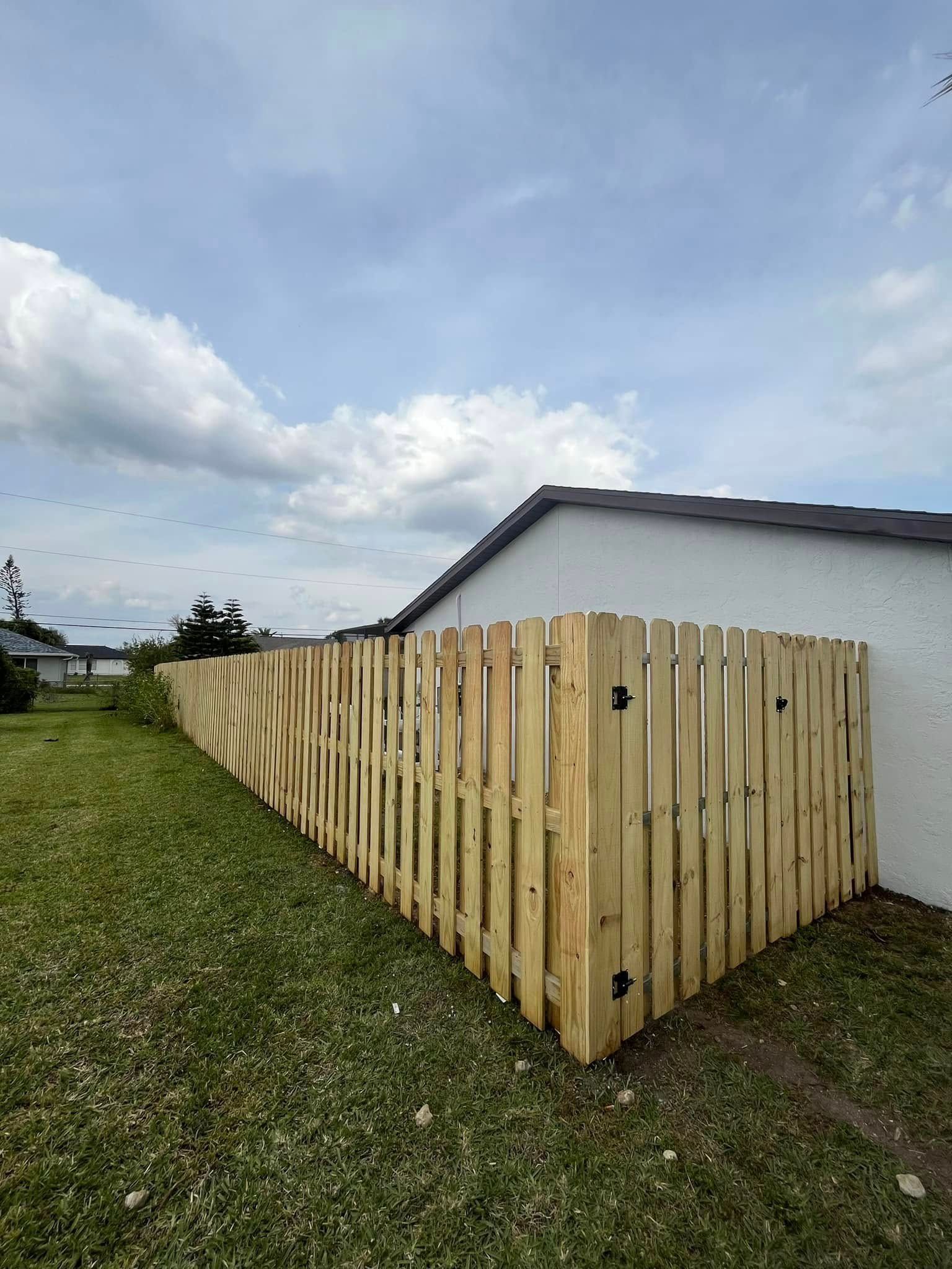 Wooden fence alongside a white house, set in green grassy yard under a cloudy sky.
