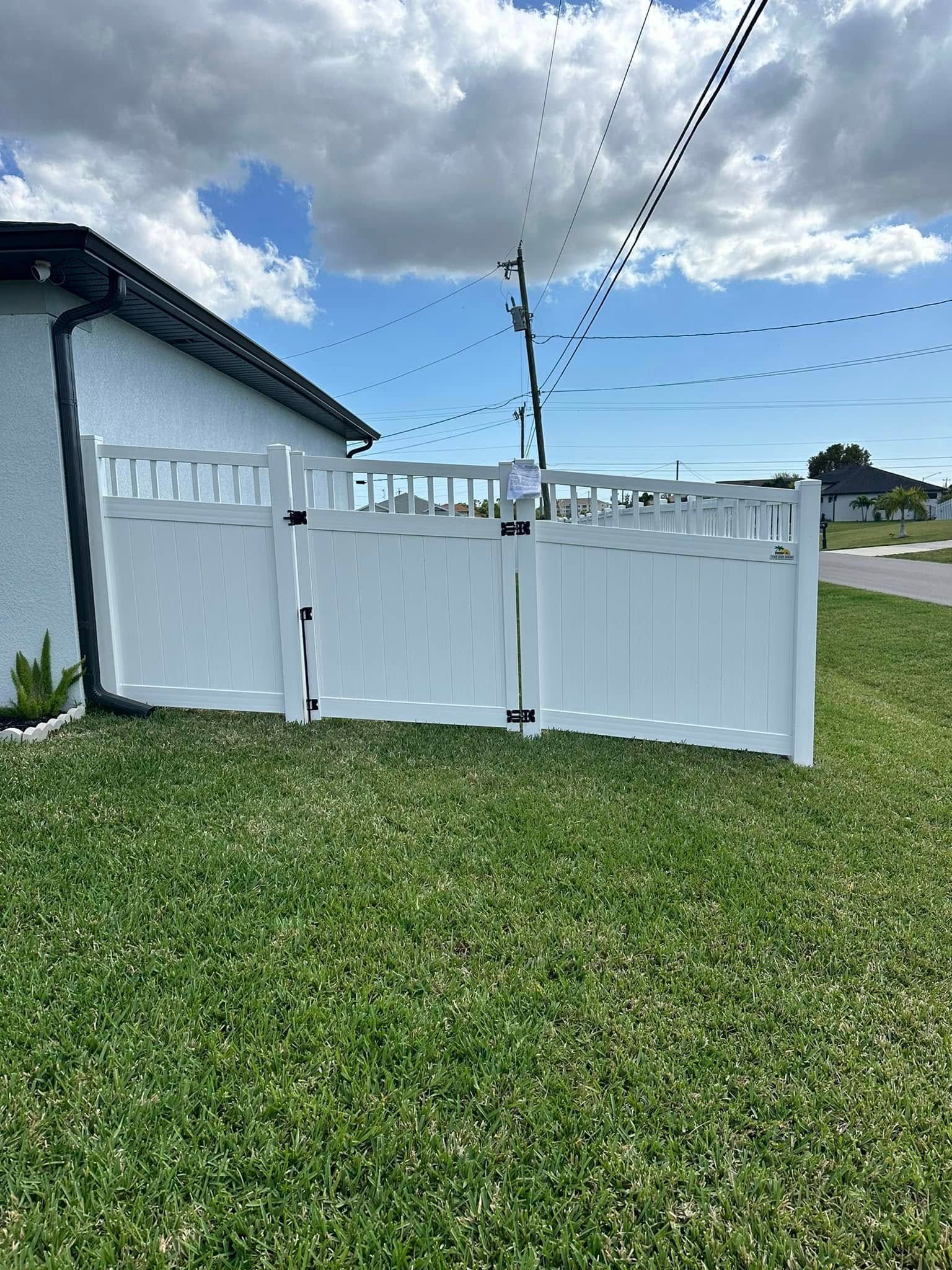 White vinyl fence surrounding a green lawn beside a building under a cloudy sky.