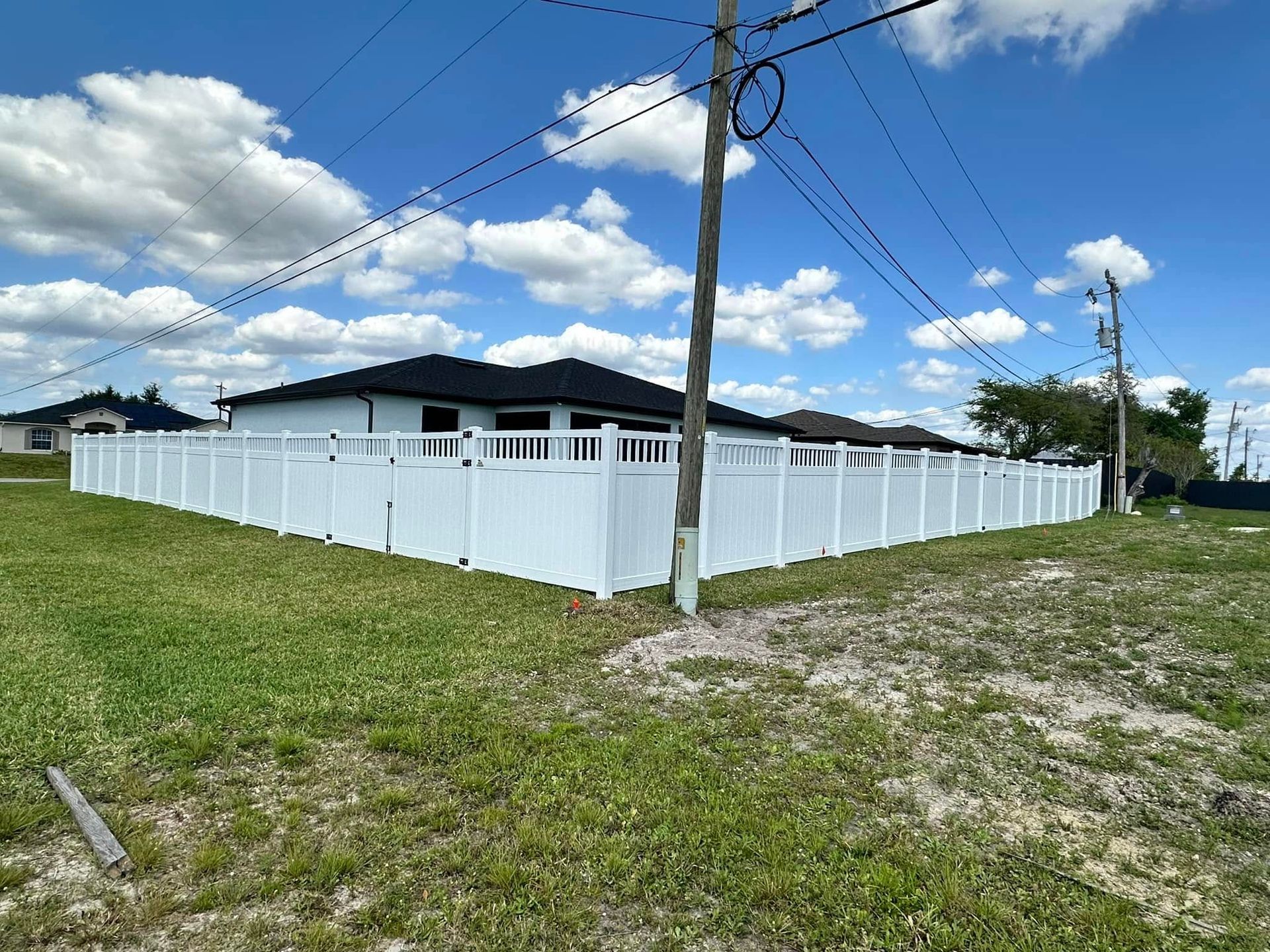 White fence around a house on a sunny day. Power lines and green grass visible.