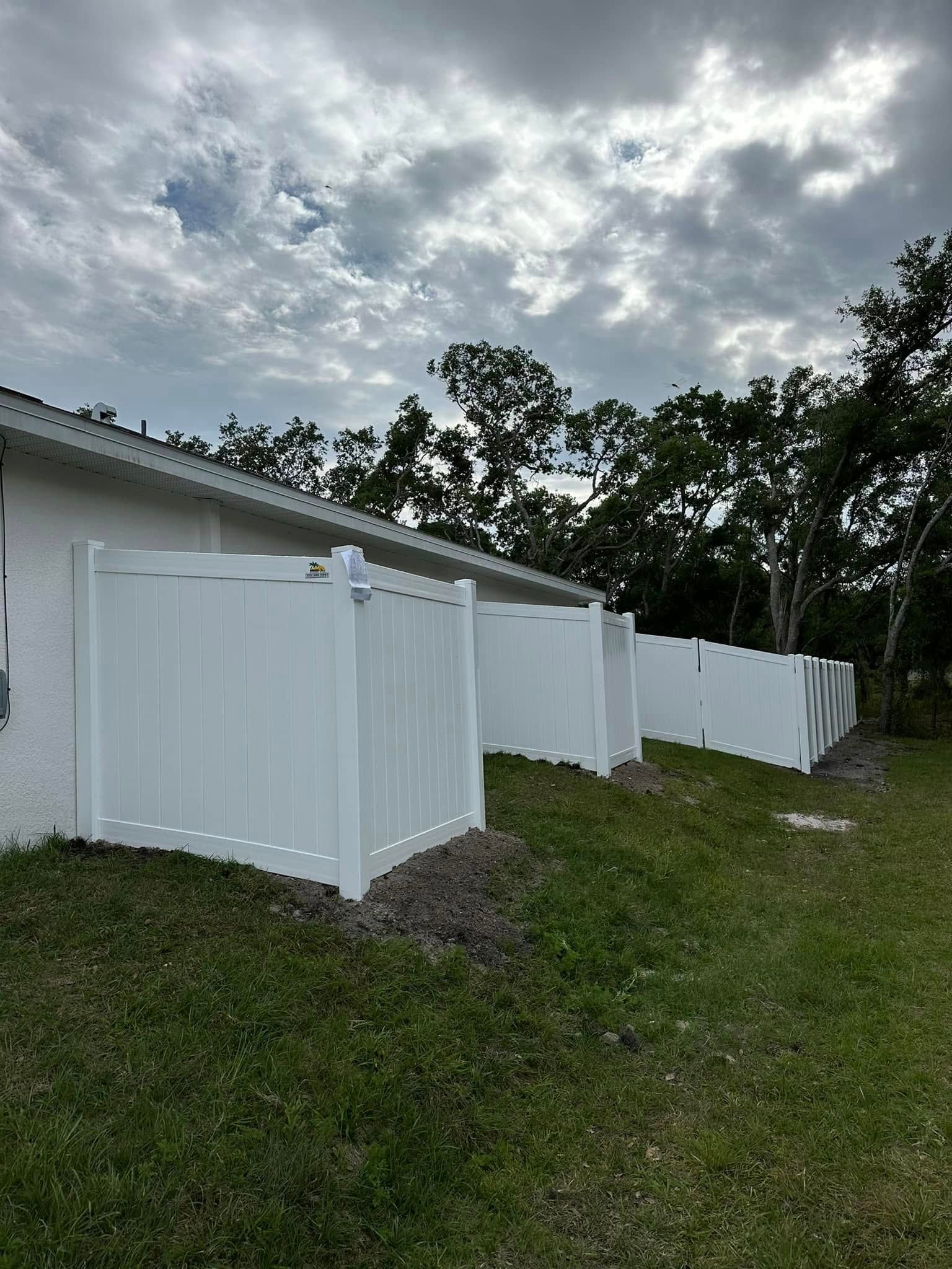 White vinyl fence along a grassy yard next to a building with a cloudy sky overhead.
