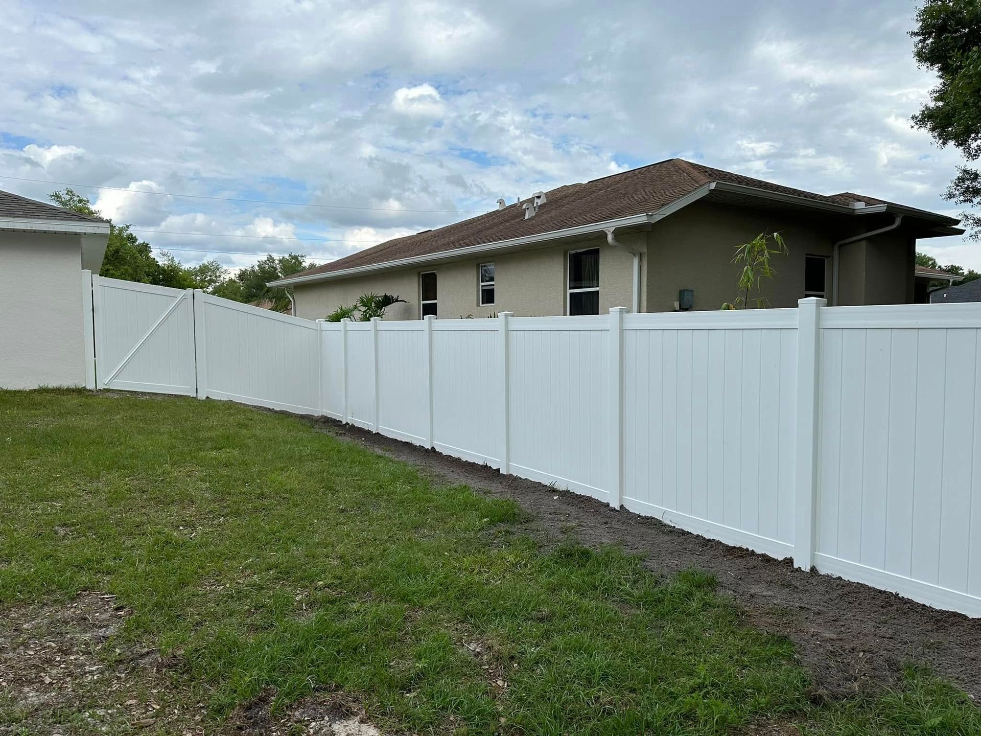 White vinyl fence surrounding a grassy yard, with a tan house in the background under a cloudy sky.