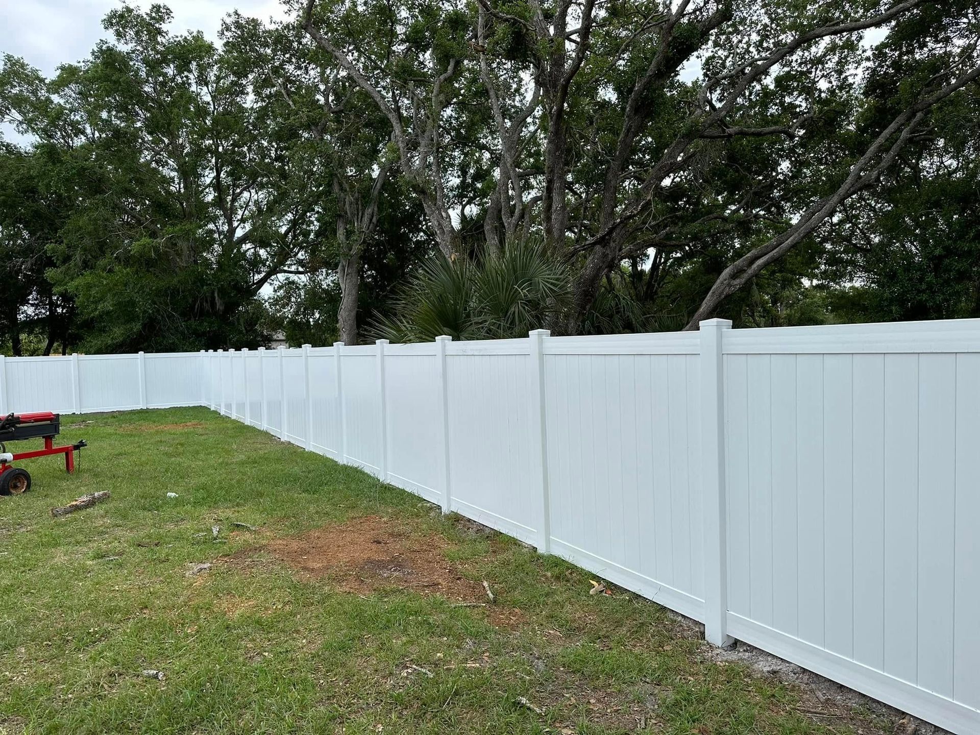 White vinyl fence bordering a grassy yard with trees in the background.