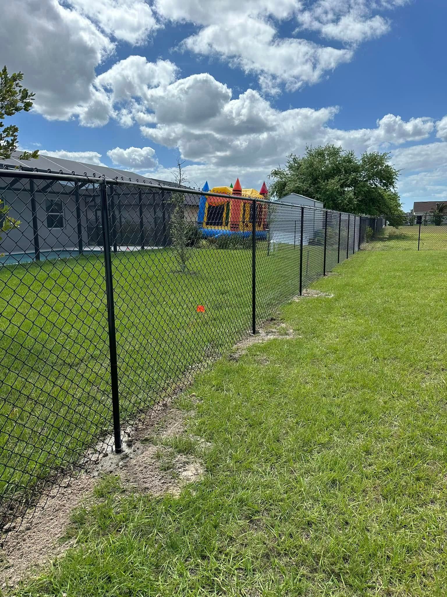 Black fence with green mesh in a grassy yard, under a cloudy blue sky.