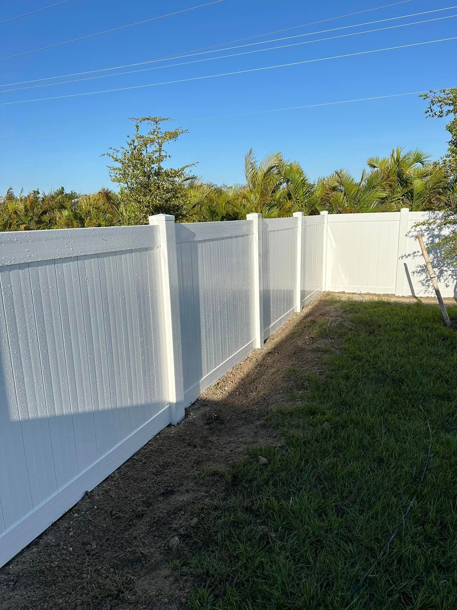 White vinyl fence in a yard with green grass and trees, under a blue sky.