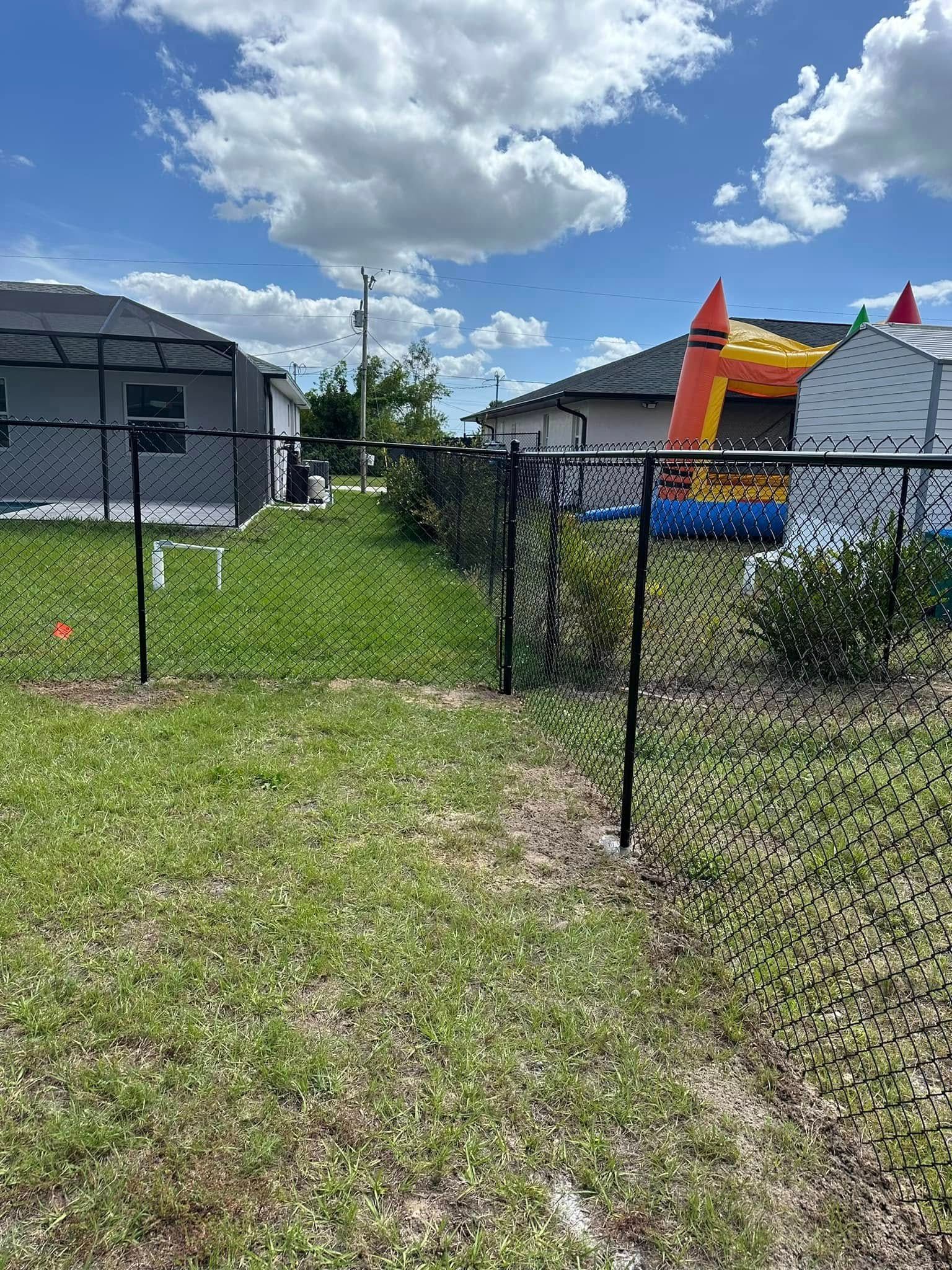Chain-link fence with an opening in a backyard; houses in the background. Cloudy sky.