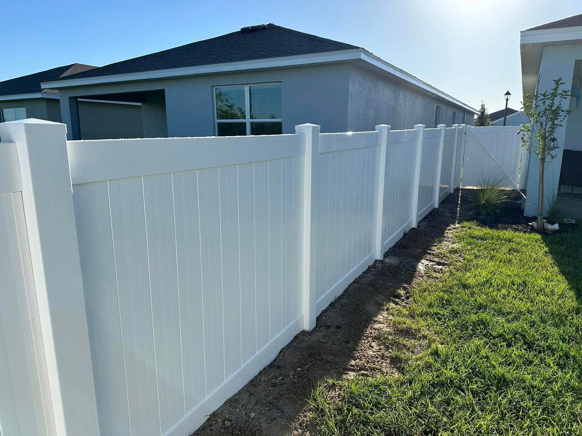 White vinyl fence in a backyard setting, separating properties.