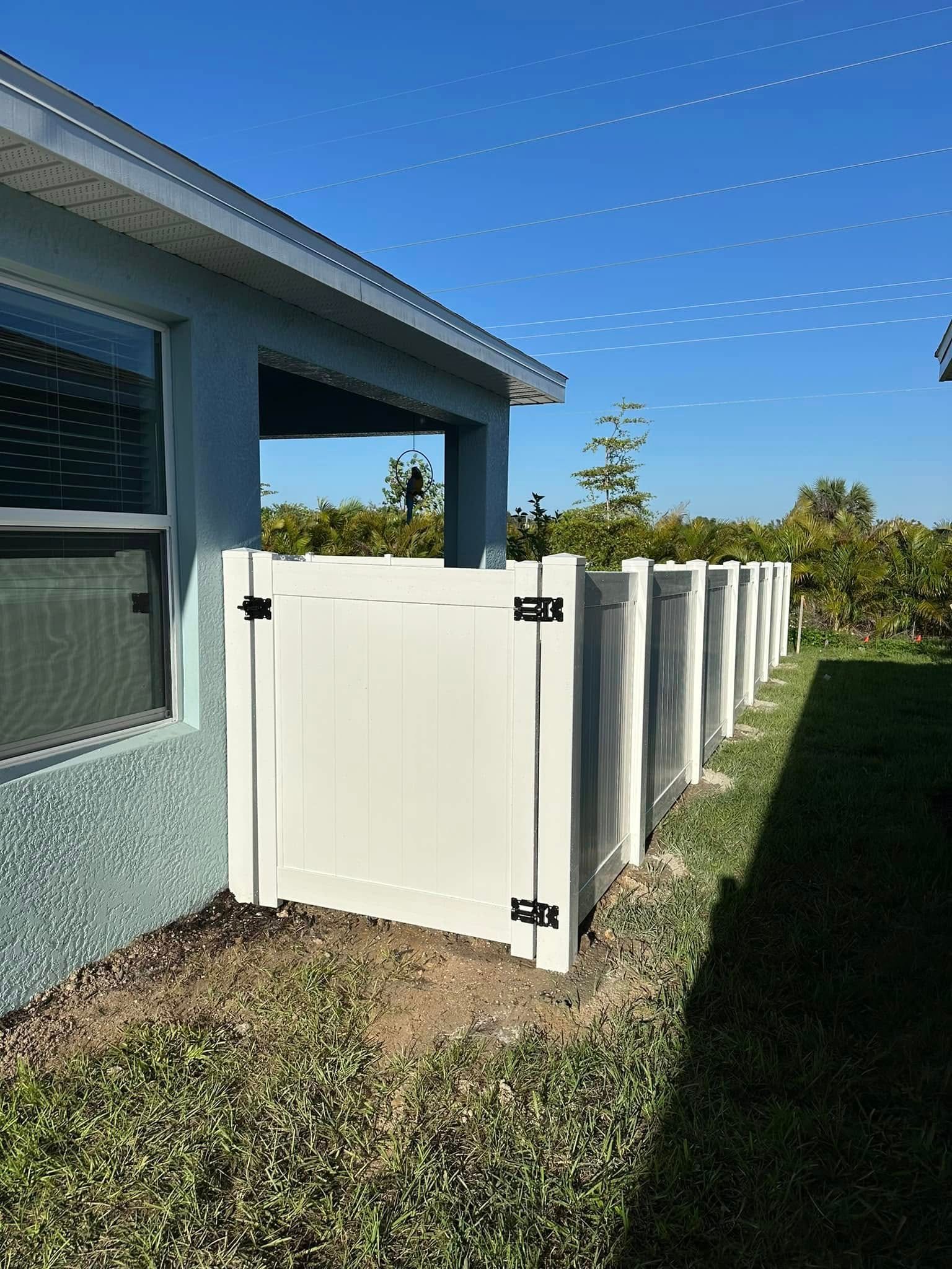 White vinyl fence attached to a light blue house, sunny outdoor setting.
