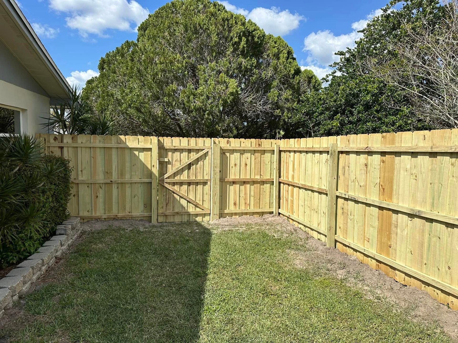 Wooden fence with gate in a backyard with grass and shrubs.
