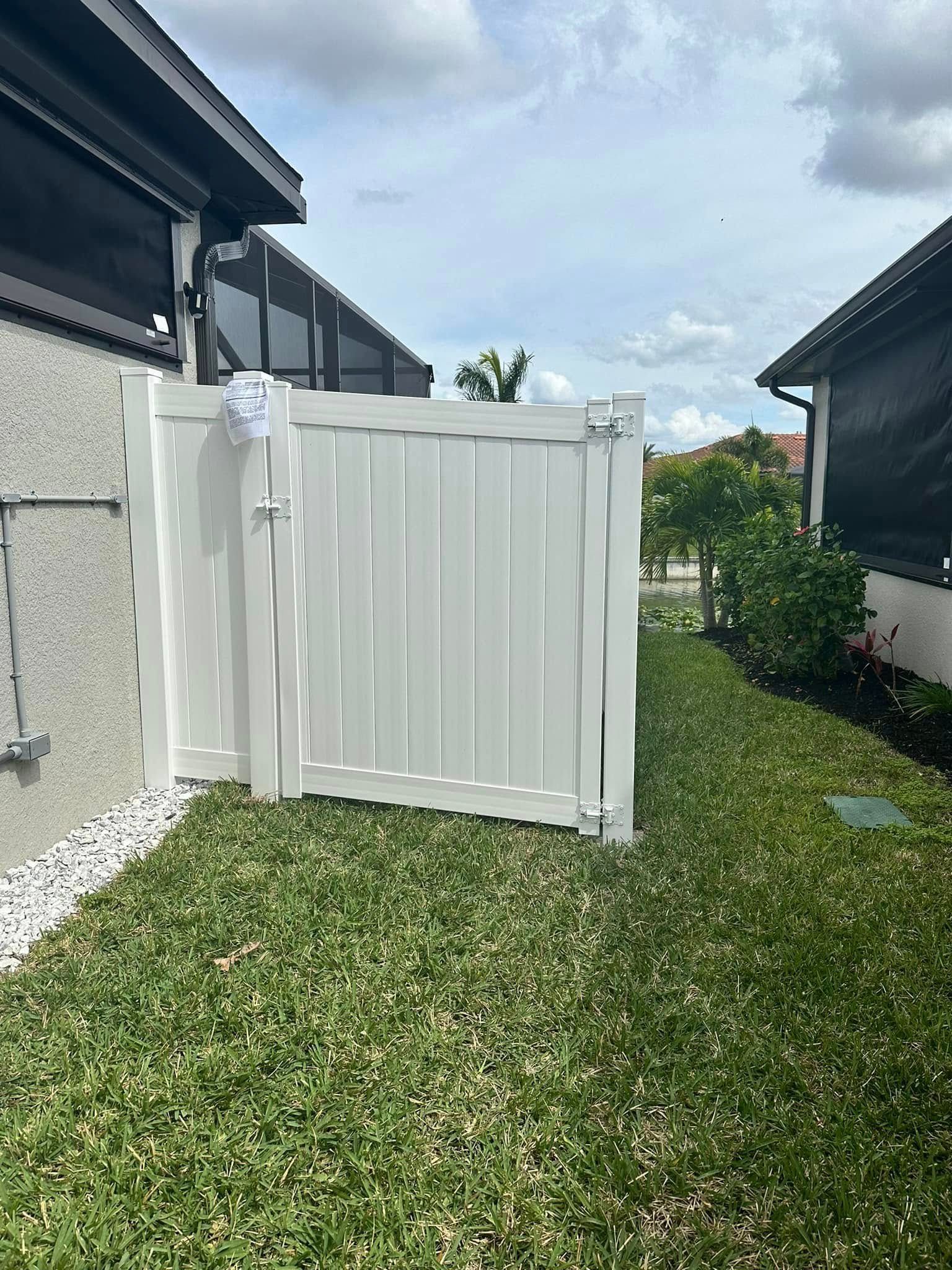 White gate between two houses, set in a grassy yard.