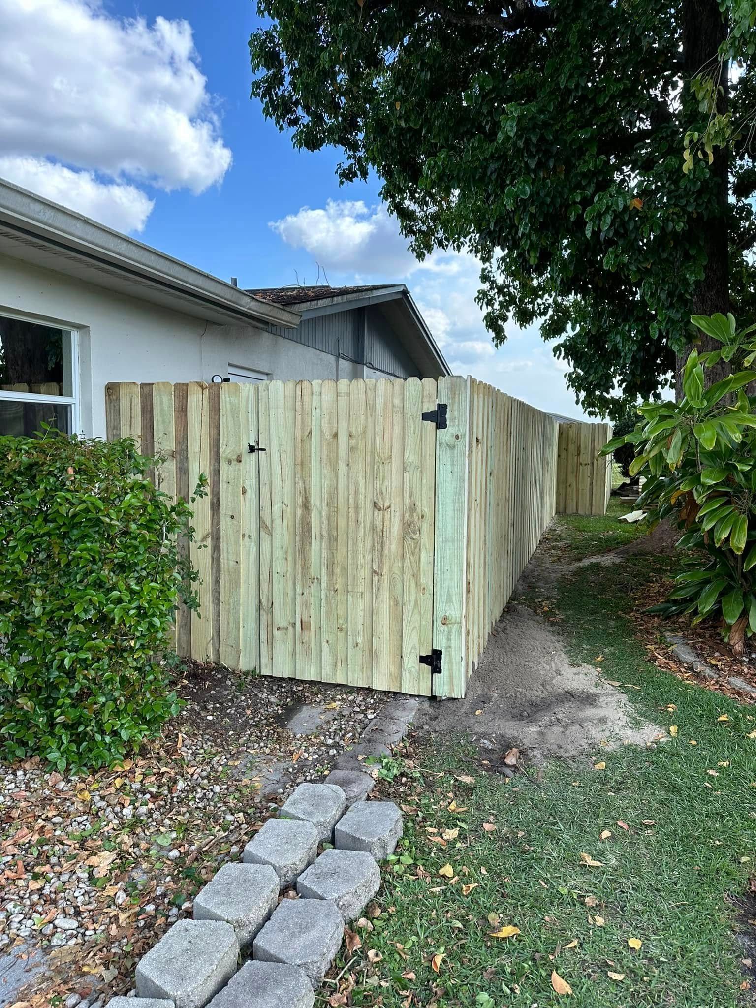 Wooden fence next to a building and greenery under a cloudy sky.