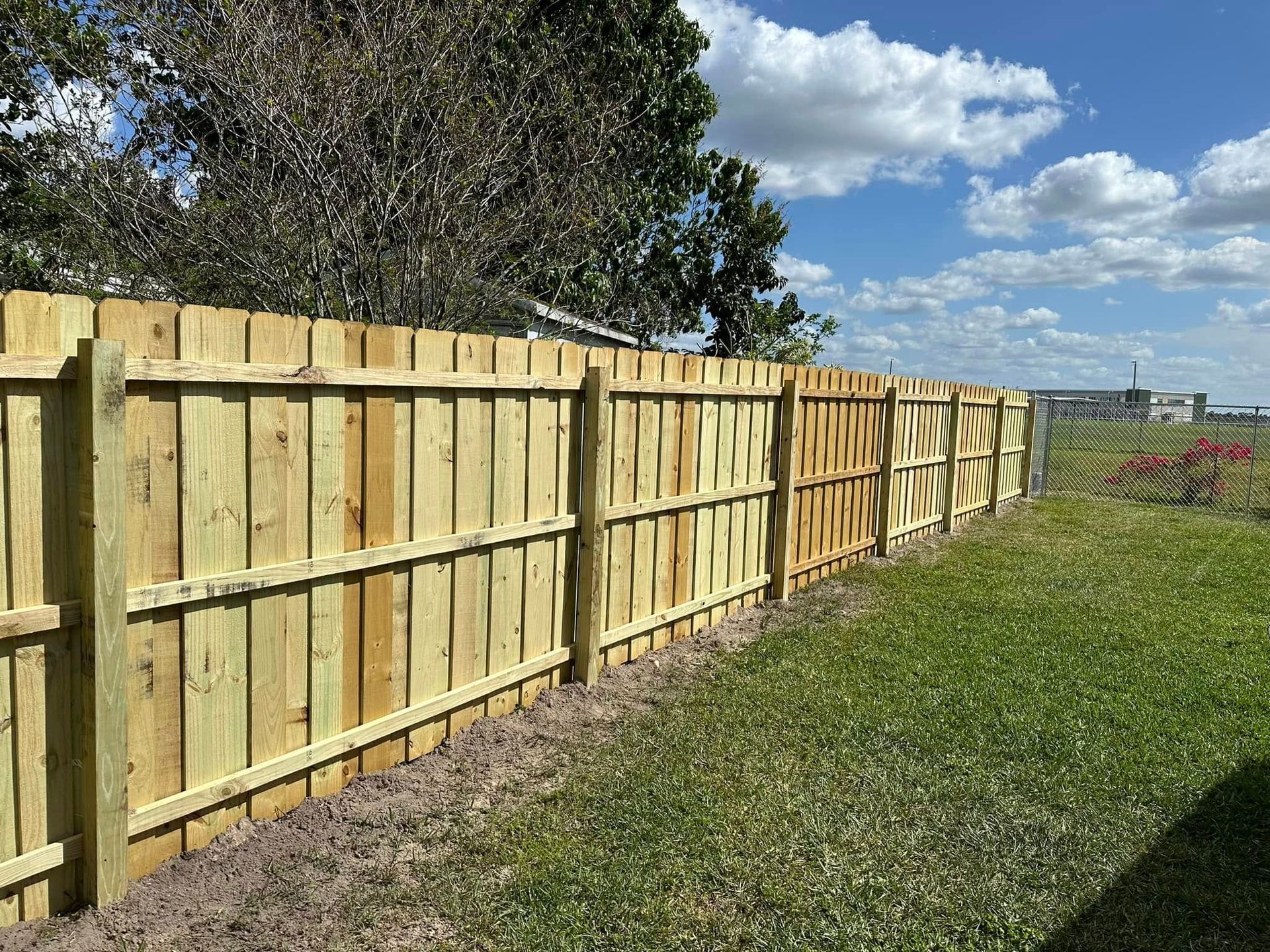 Wooden fence in a grassy yard under a blue sky with clouds.