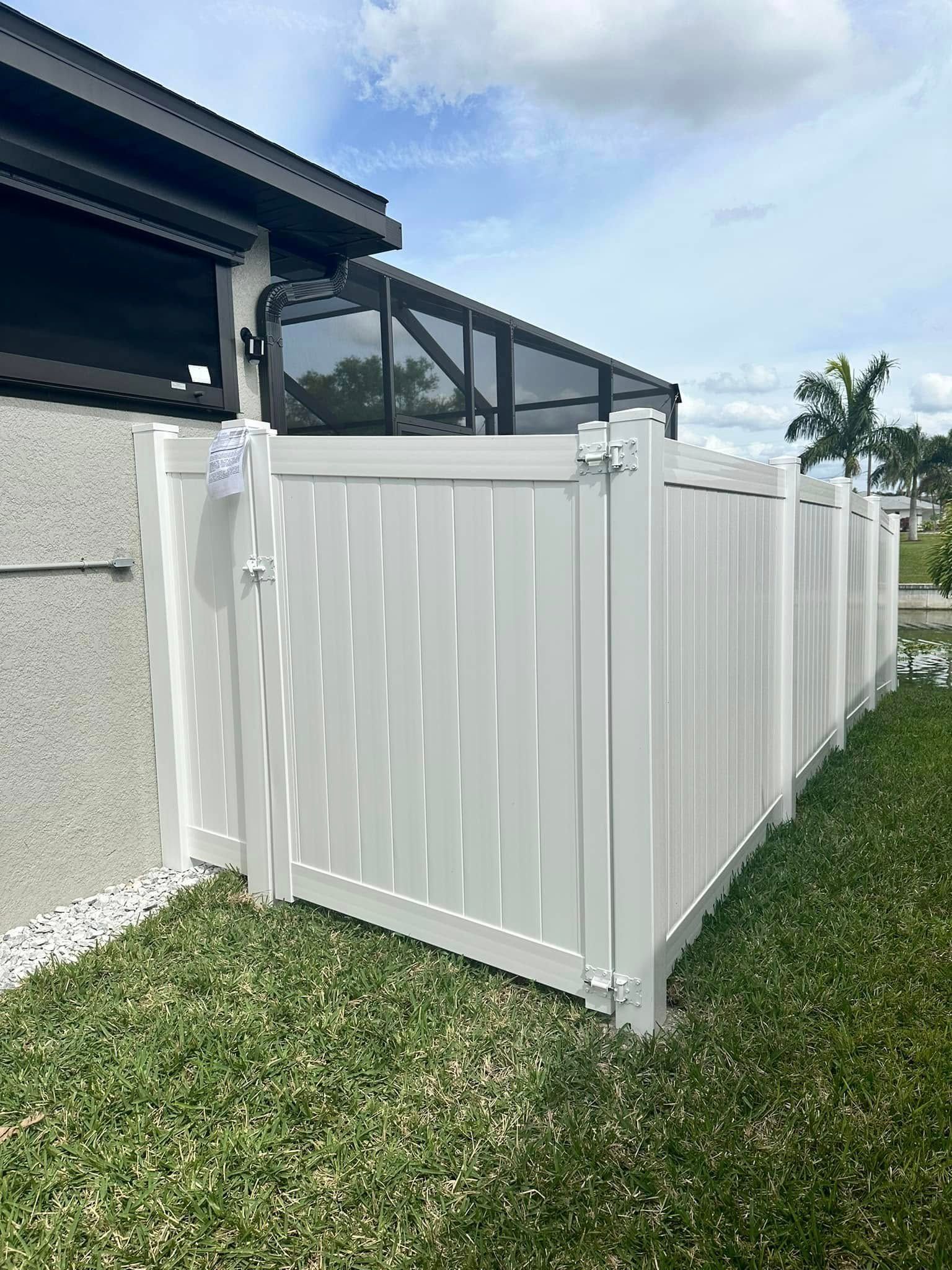 White vinyl fence with gate in a backyard, next to a house with a screened patio.