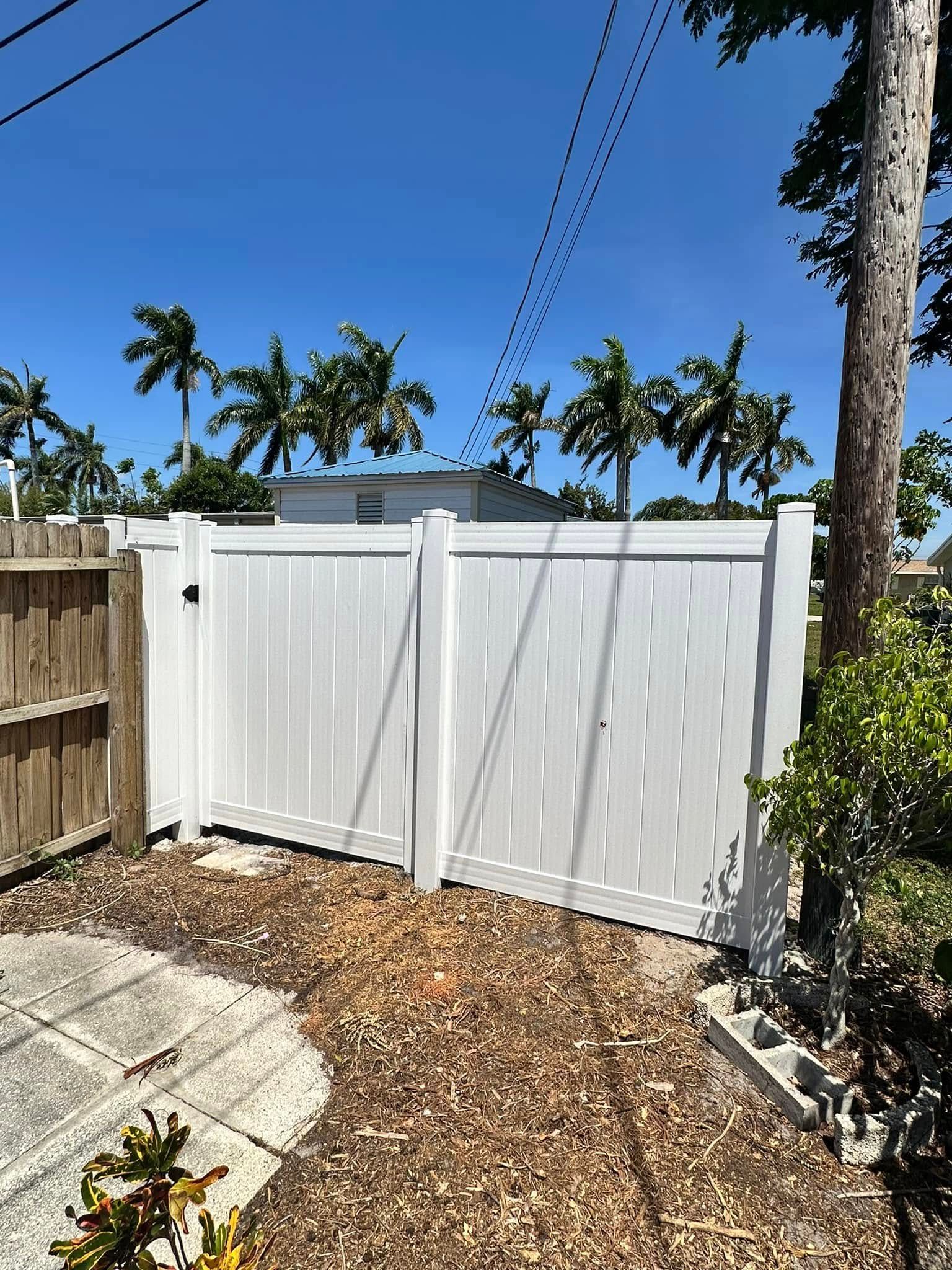White vinyl double gate in a yard with palm trees and blue sky.