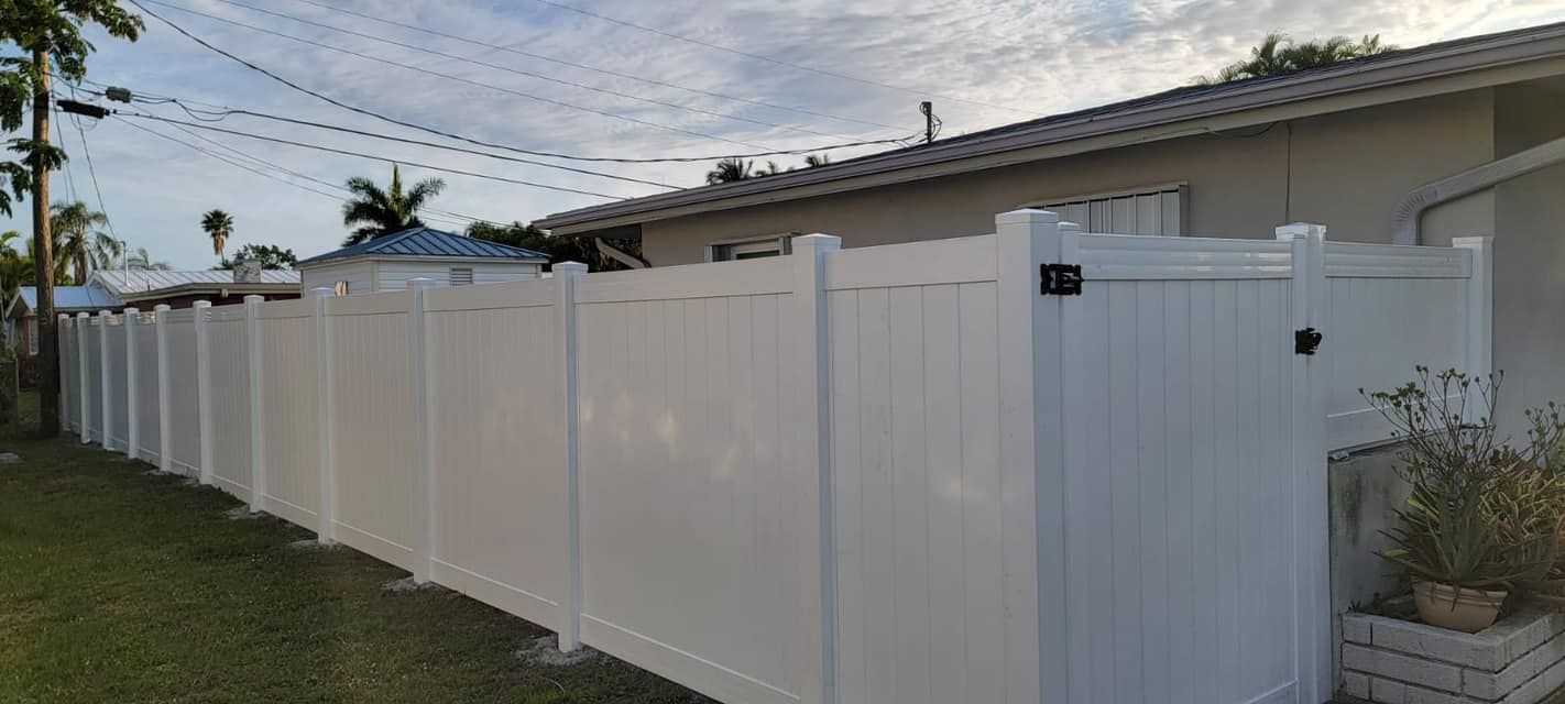 White fence bordering a grassy yard. Houses are in the background under a cloudy sky.