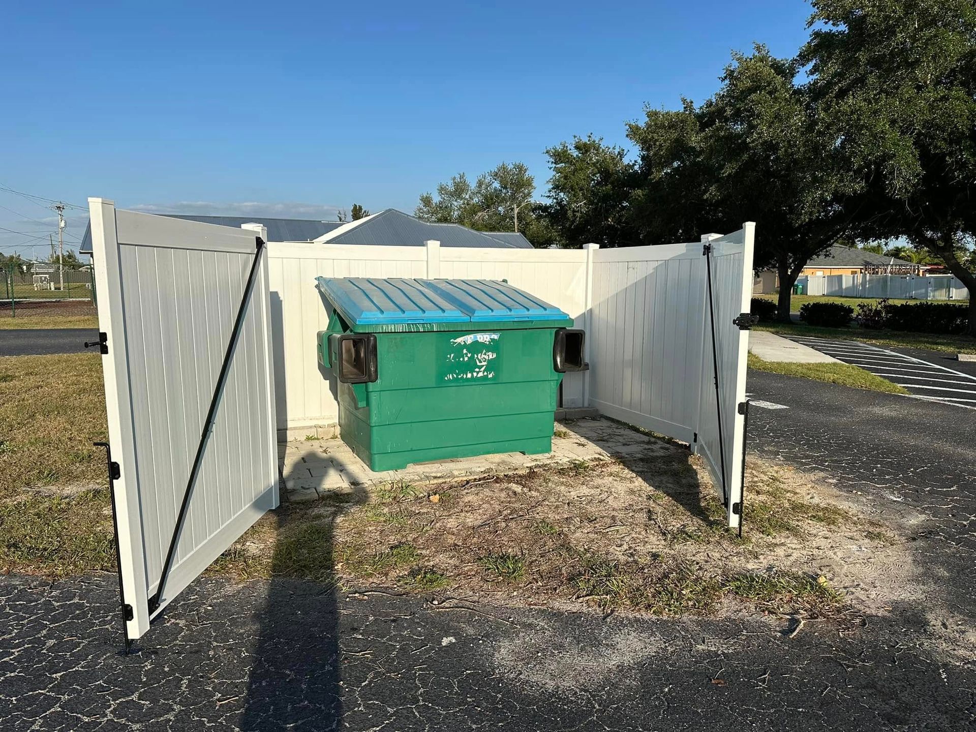 Green dumpster enclosed by white wooden fence.