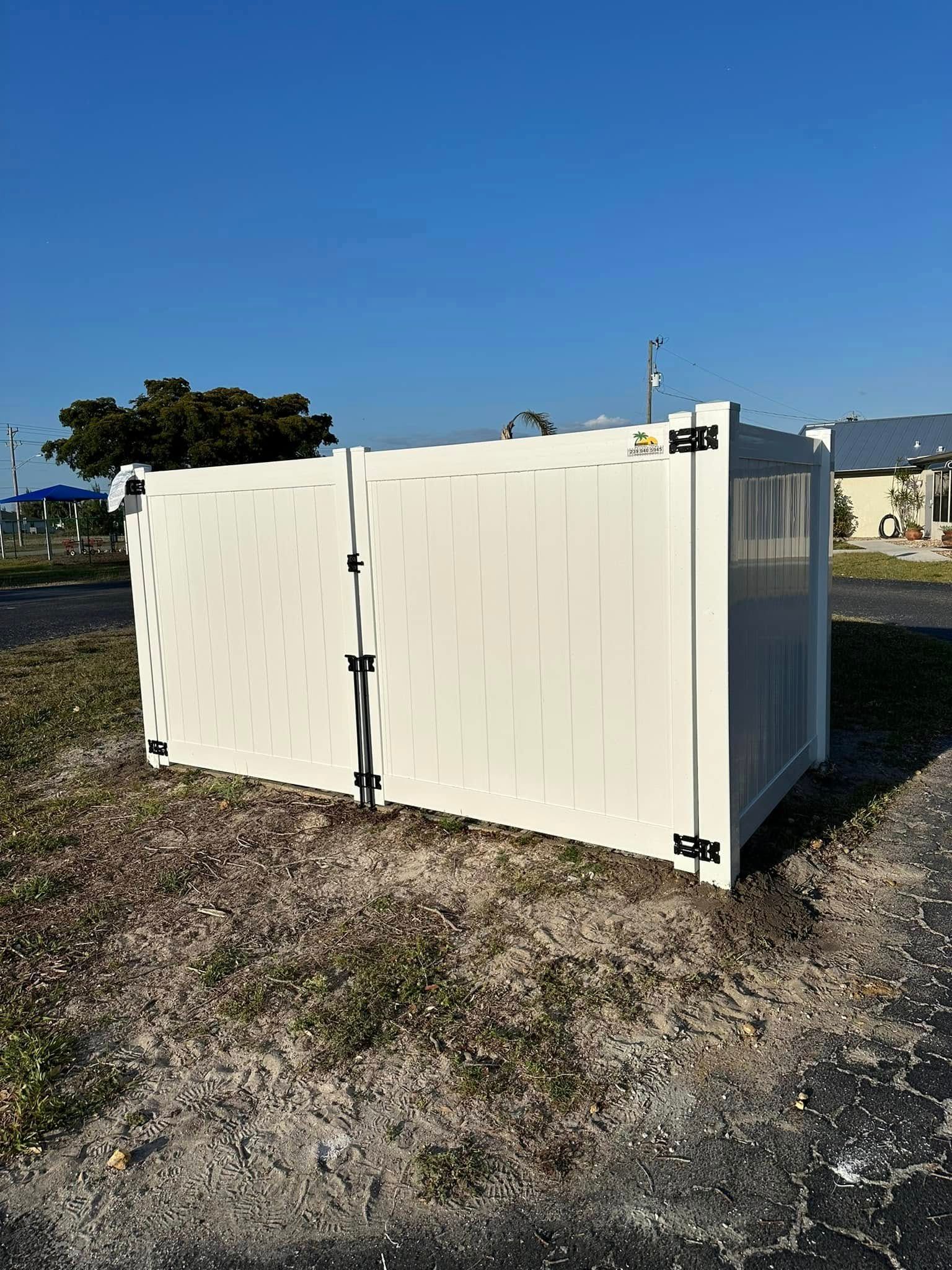 White vinyl fence enclosure outdoors on a sunny day; hinges and latch visible.