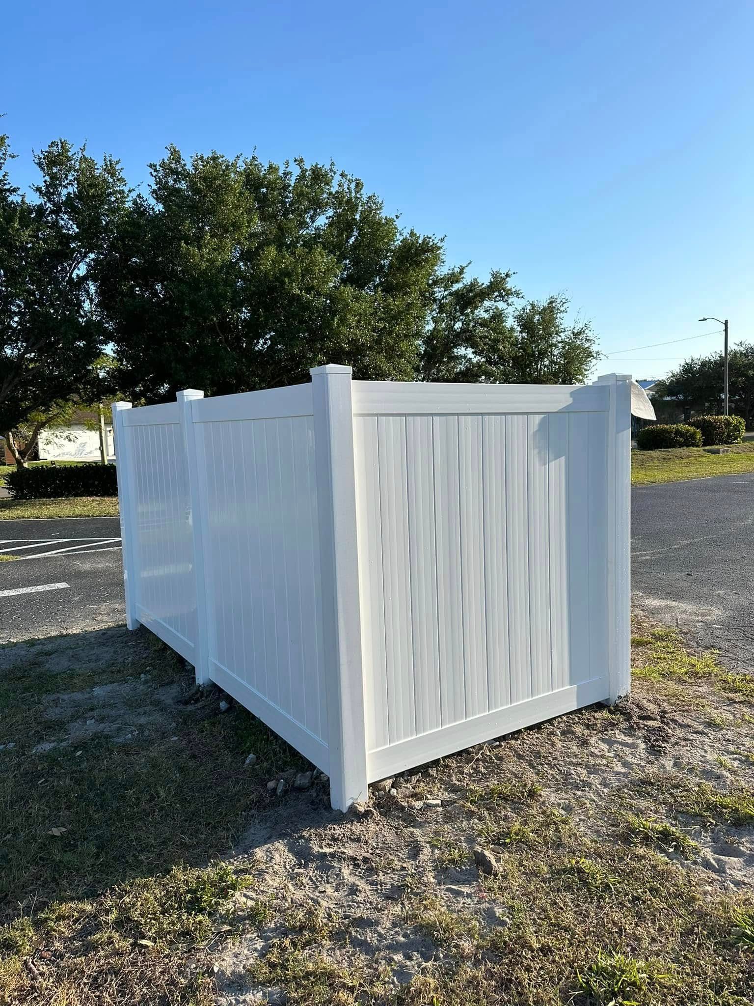 White vinyl fence in an outdoor setting with trees and blue sky.