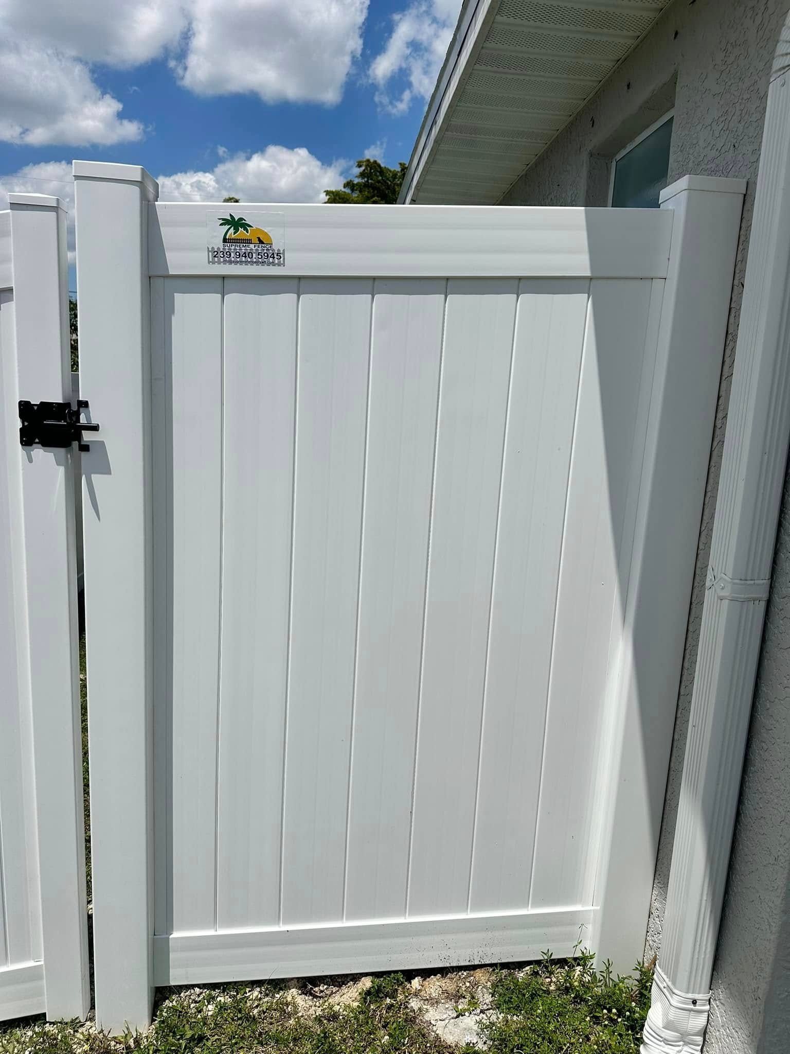 White vinyl fence gate with latch, next to a house, on a sunny day.