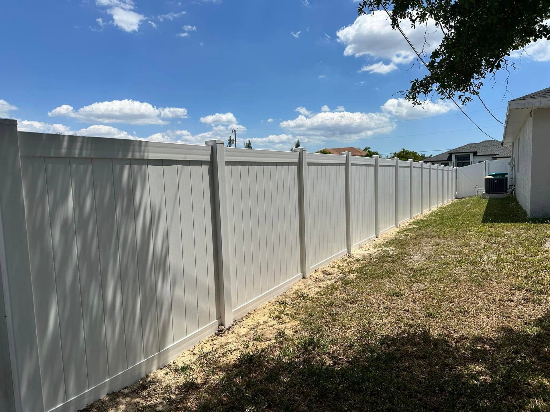 White vinyl fence in a backyard under a blue sky with scattered clouds.