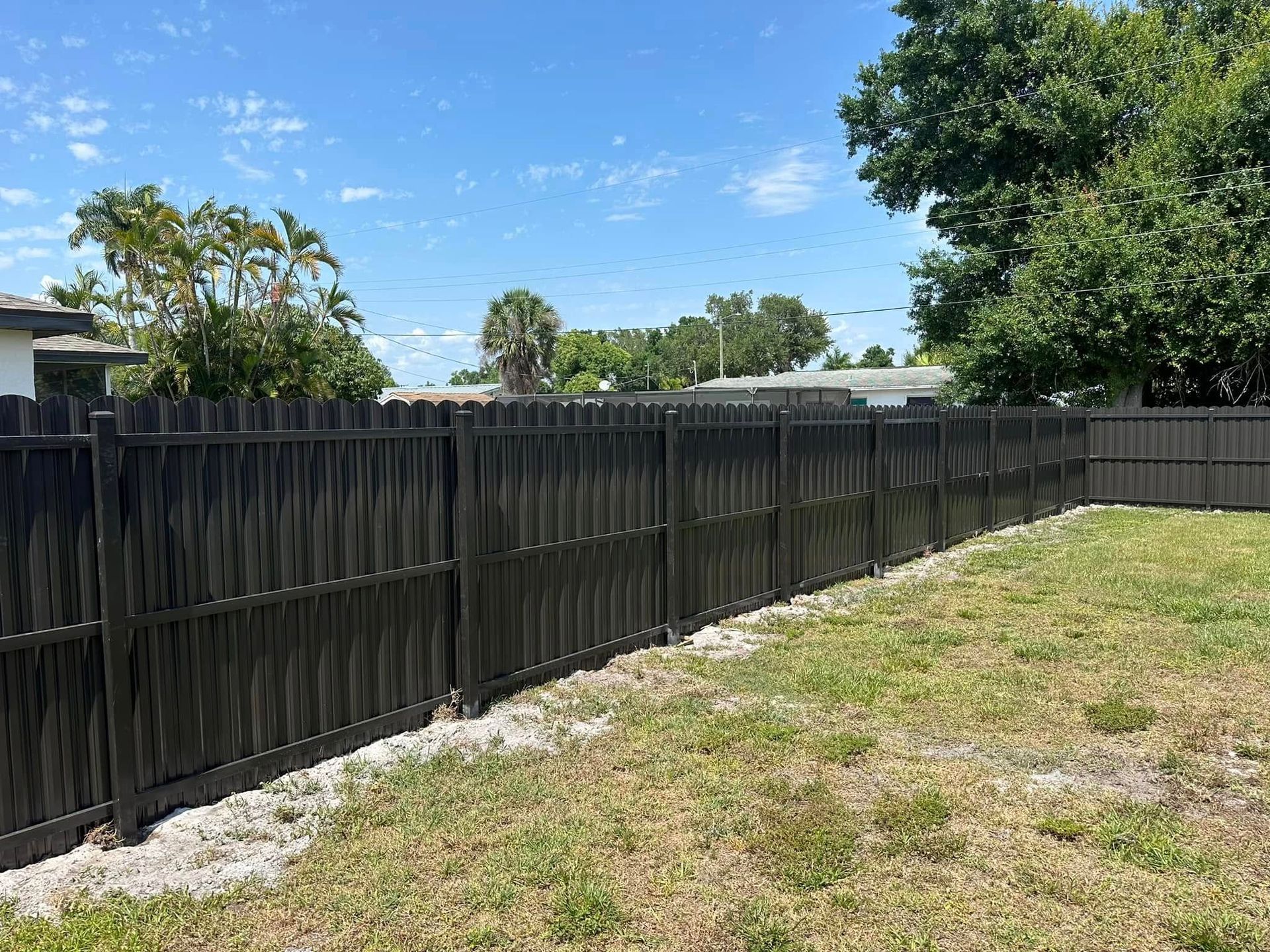 Black wooden fence in a backyard under a blue sky with trees.