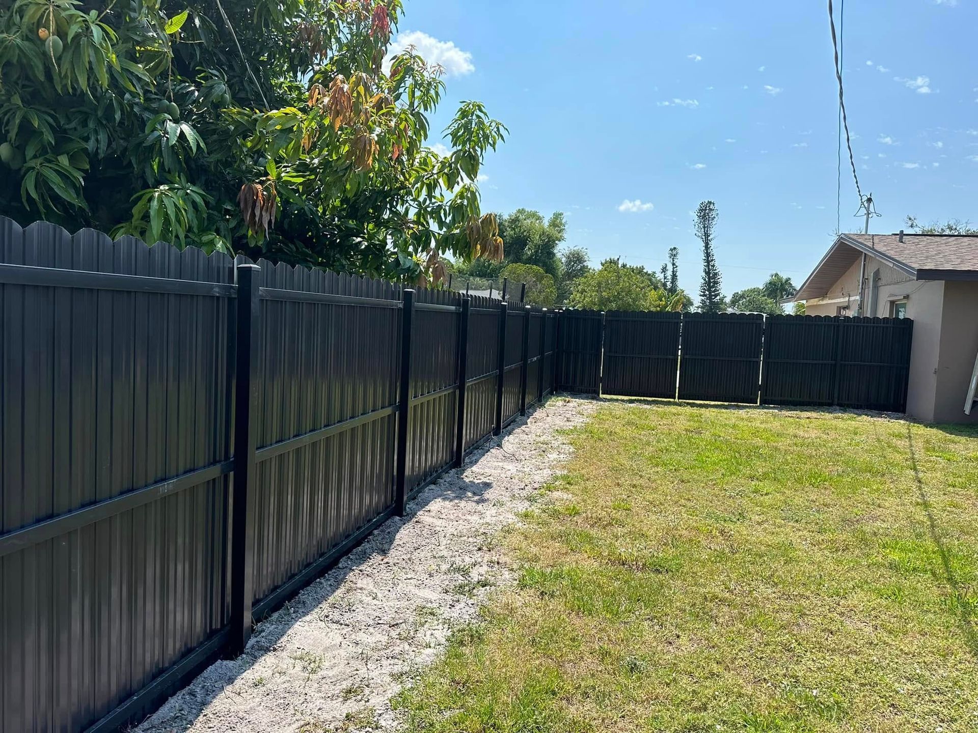 Black privacy fence along a grassy yard, under a sunny sky.