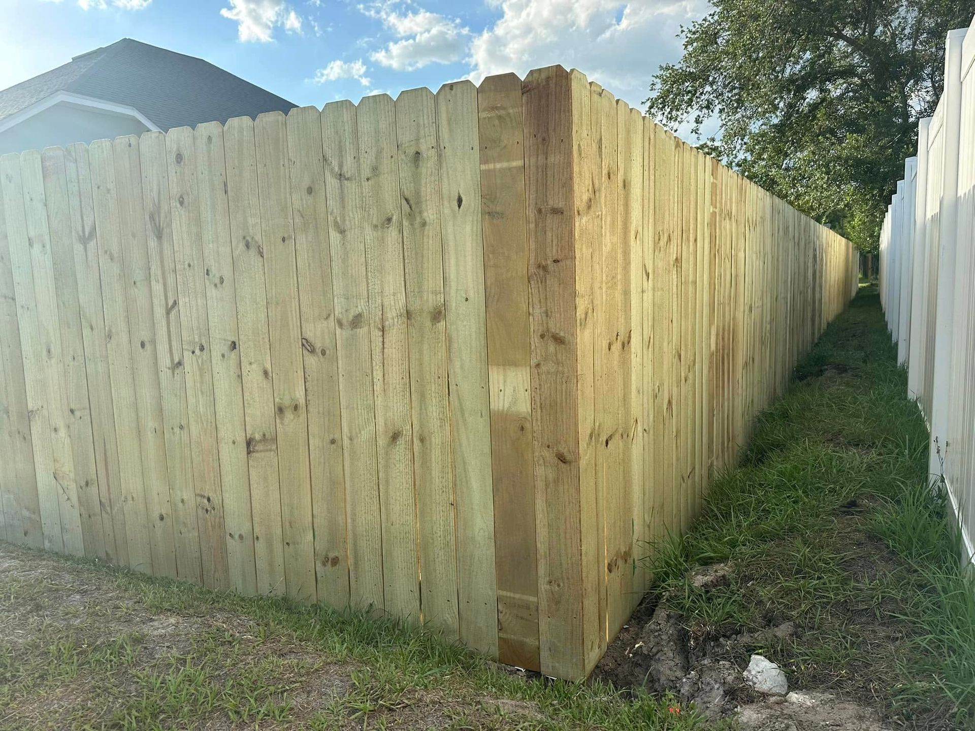 Wooden privacy fence corner, light brown, against blue sky and white fence.