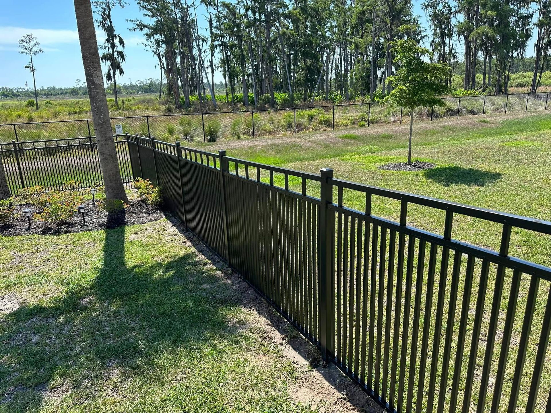 Black metal fence in a grassy yard, with trees and vegetation in the background.