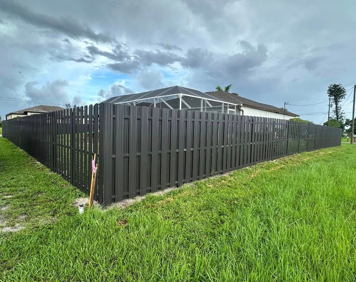 Black wooden fence surrounding a backyard with green grass under a cloudy sky.