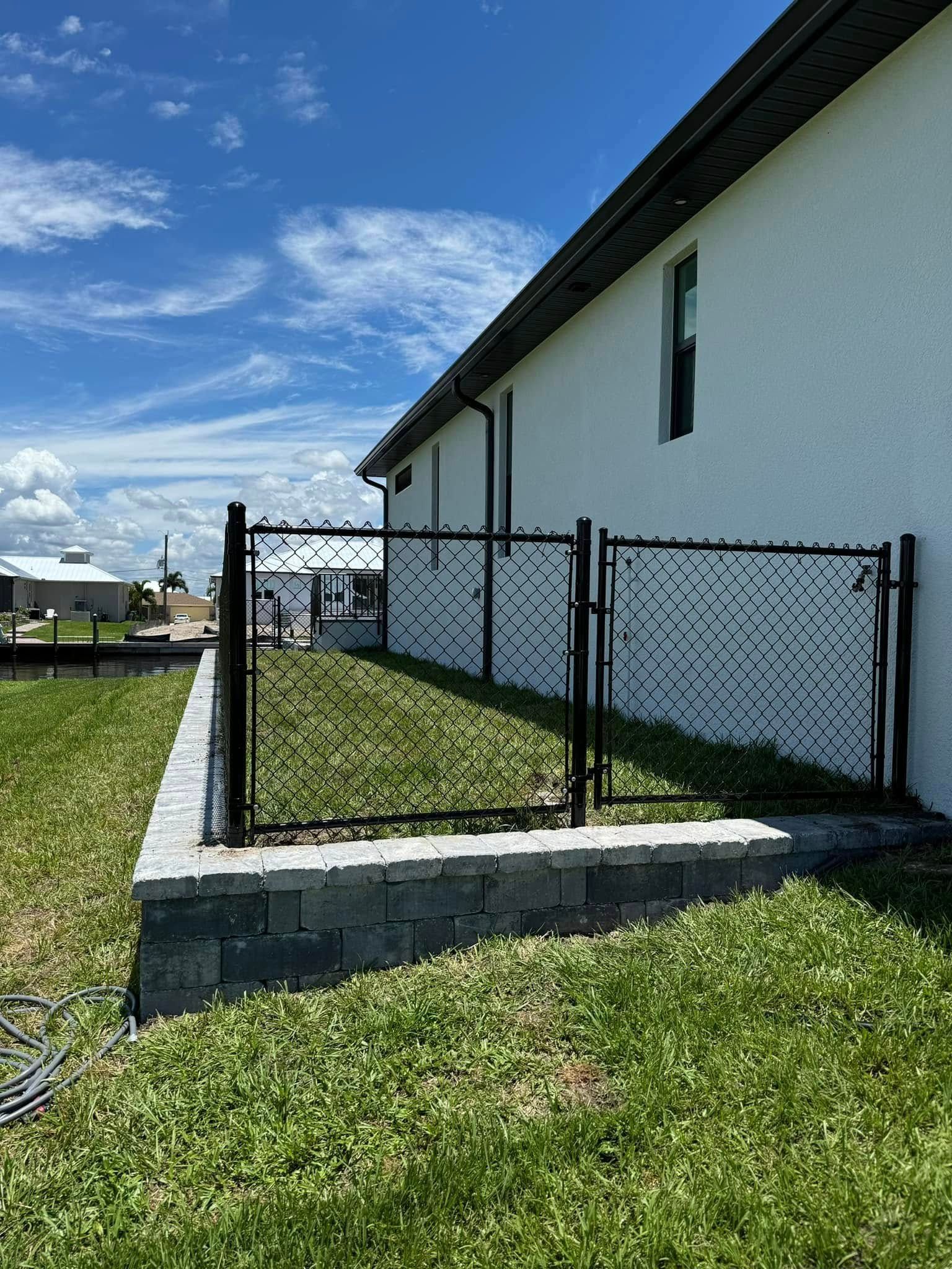 Black decorative fence on a retaining wall next to a white building on a grassy lawn.
