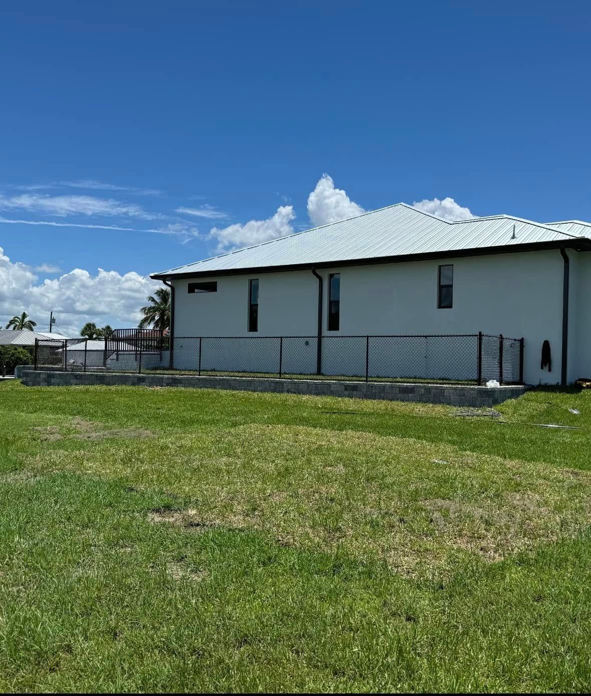 A white house with a chain link fence, against a backdrop of blue sky and green grass.