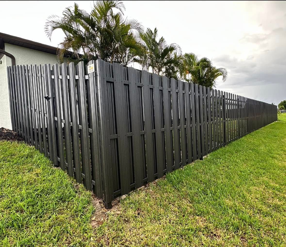 Black wooden fence around a yard; green grass and a cloudy sky.