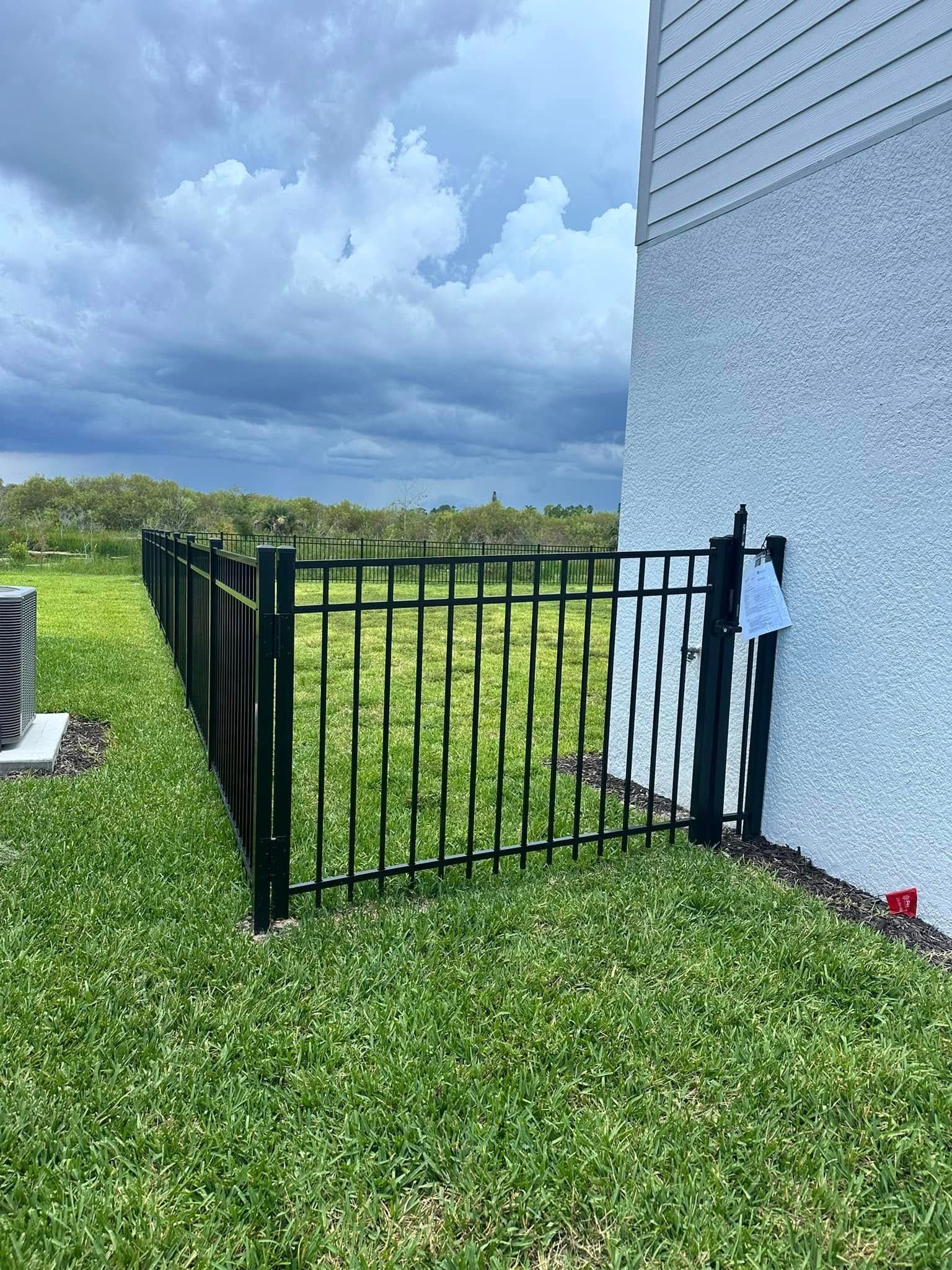 Black metal fence next to a house, enclosing a grassy yard under a cloudy sky.