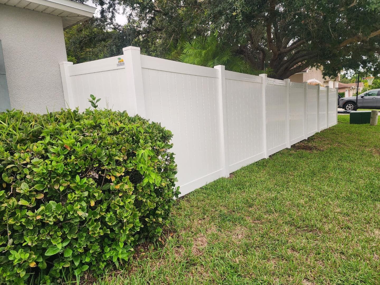 White vinyl fence bordering a grassy lawn and trimmed hedge.