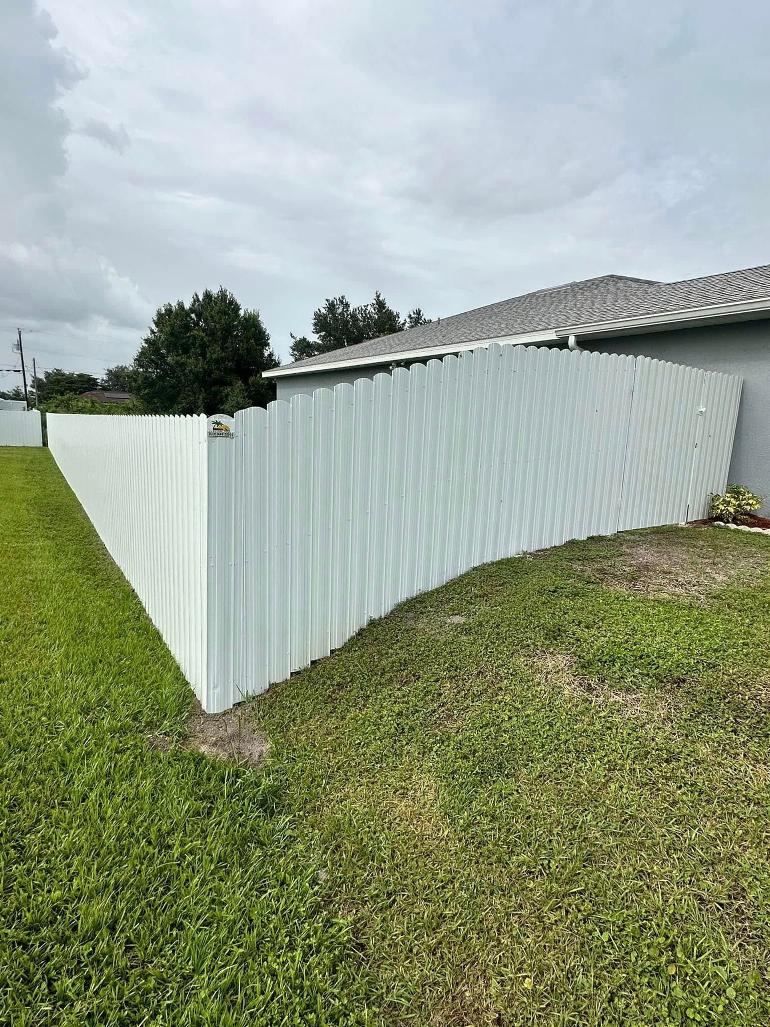 White picket fence in a yard with green grass, under a cloudy sky.