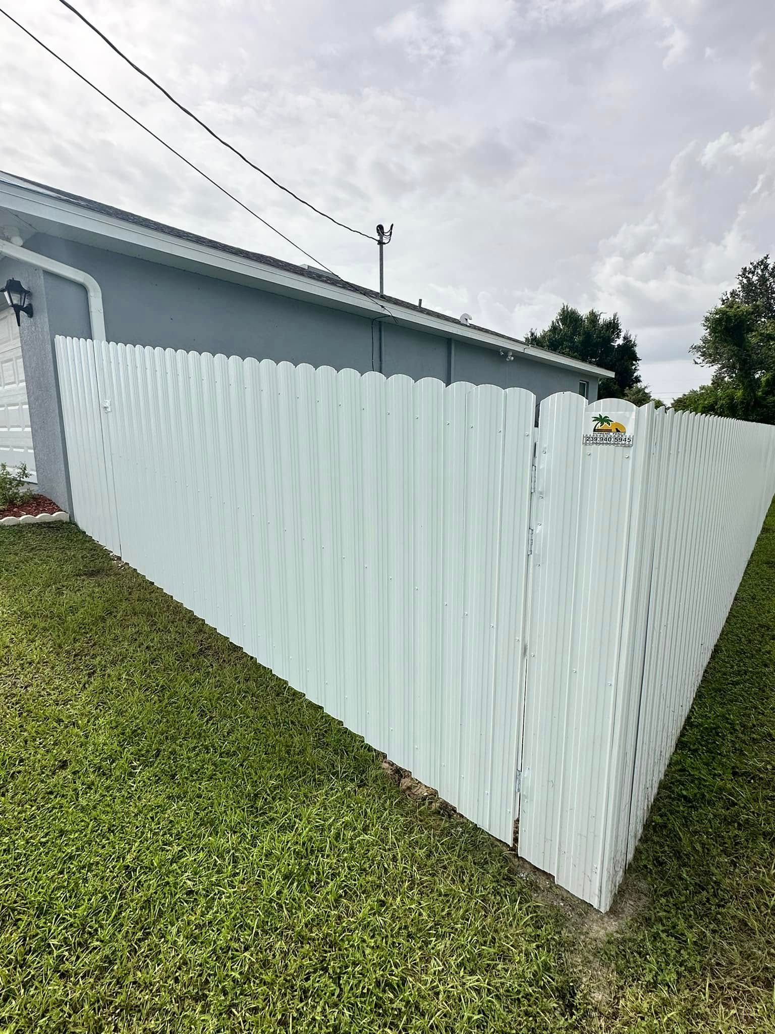 White vinyl fence bordering a grassy yard, next to a light blue house under a cloudy sky.
