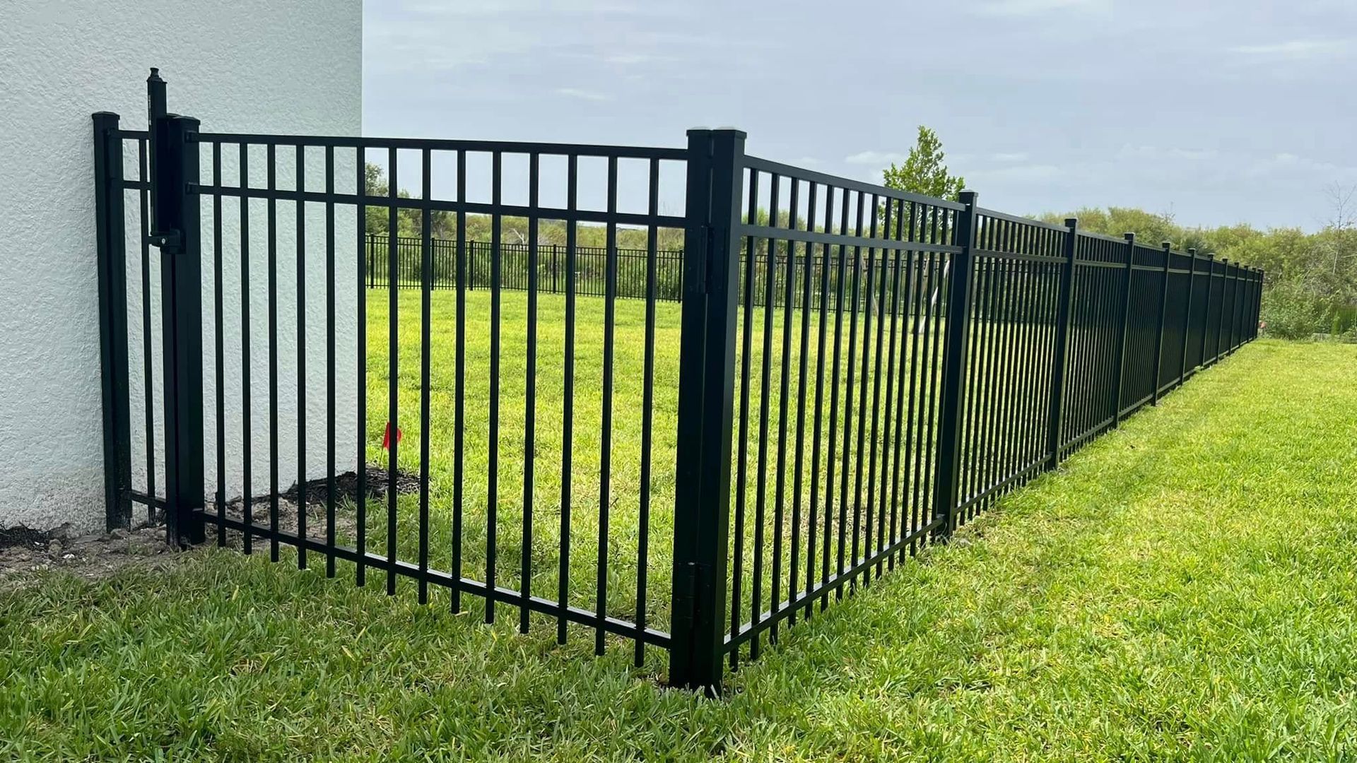 Black metal fence bordering a grassy yard. Green camouflage netting is attached on the right side.