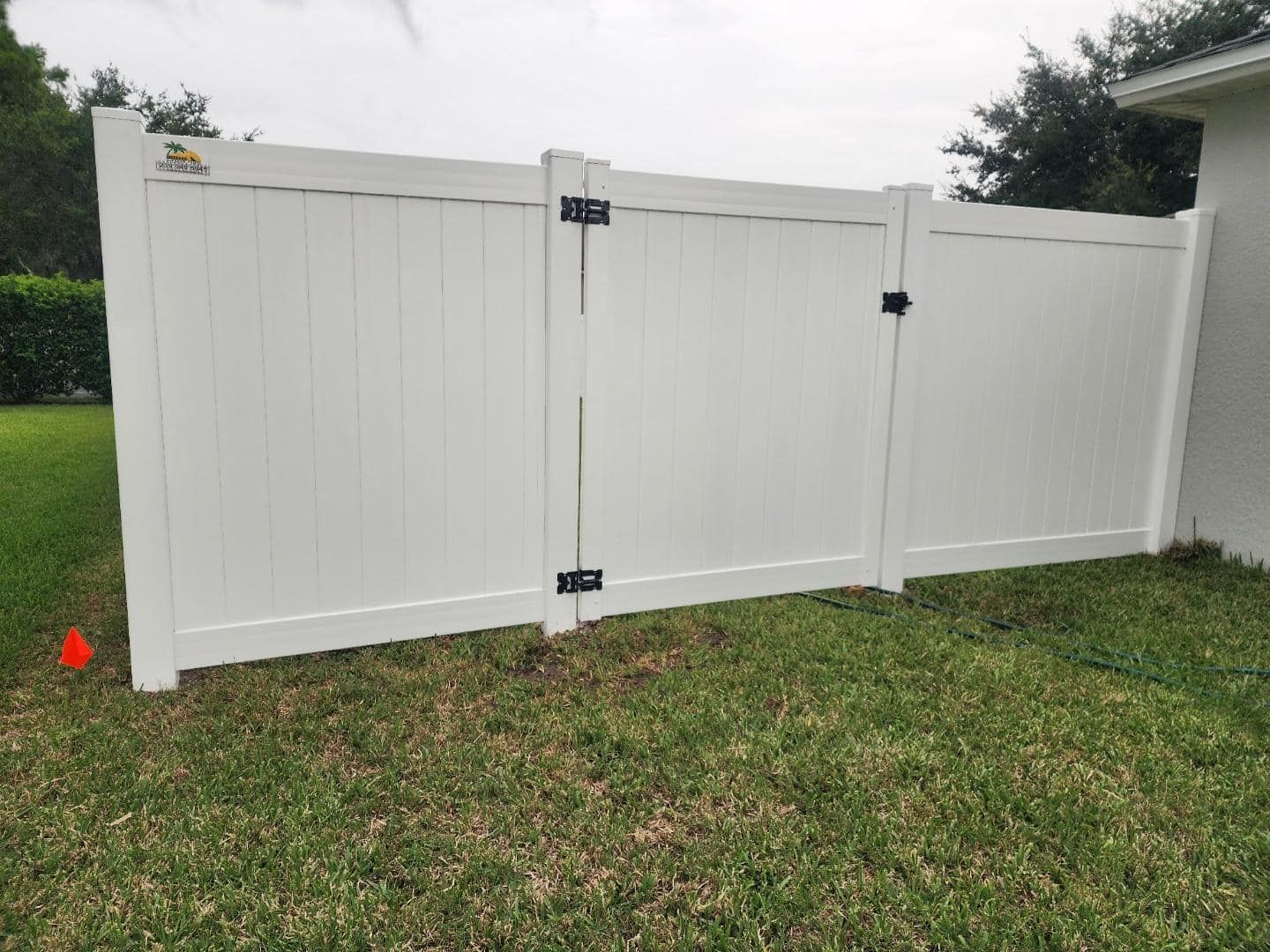 White vinyl fence with a gate in a grassy yard next to a house.