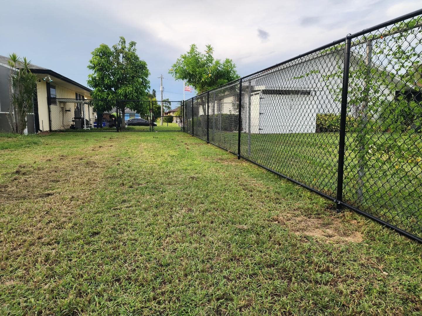 Black chain-link fence in a yard, next to a house. Overcast sky.