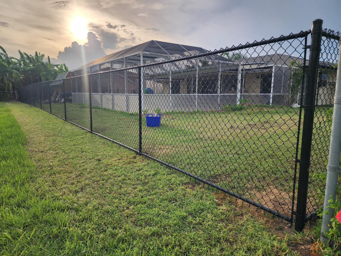 Black chain link fence surrounding a house with a sunlit sky above.