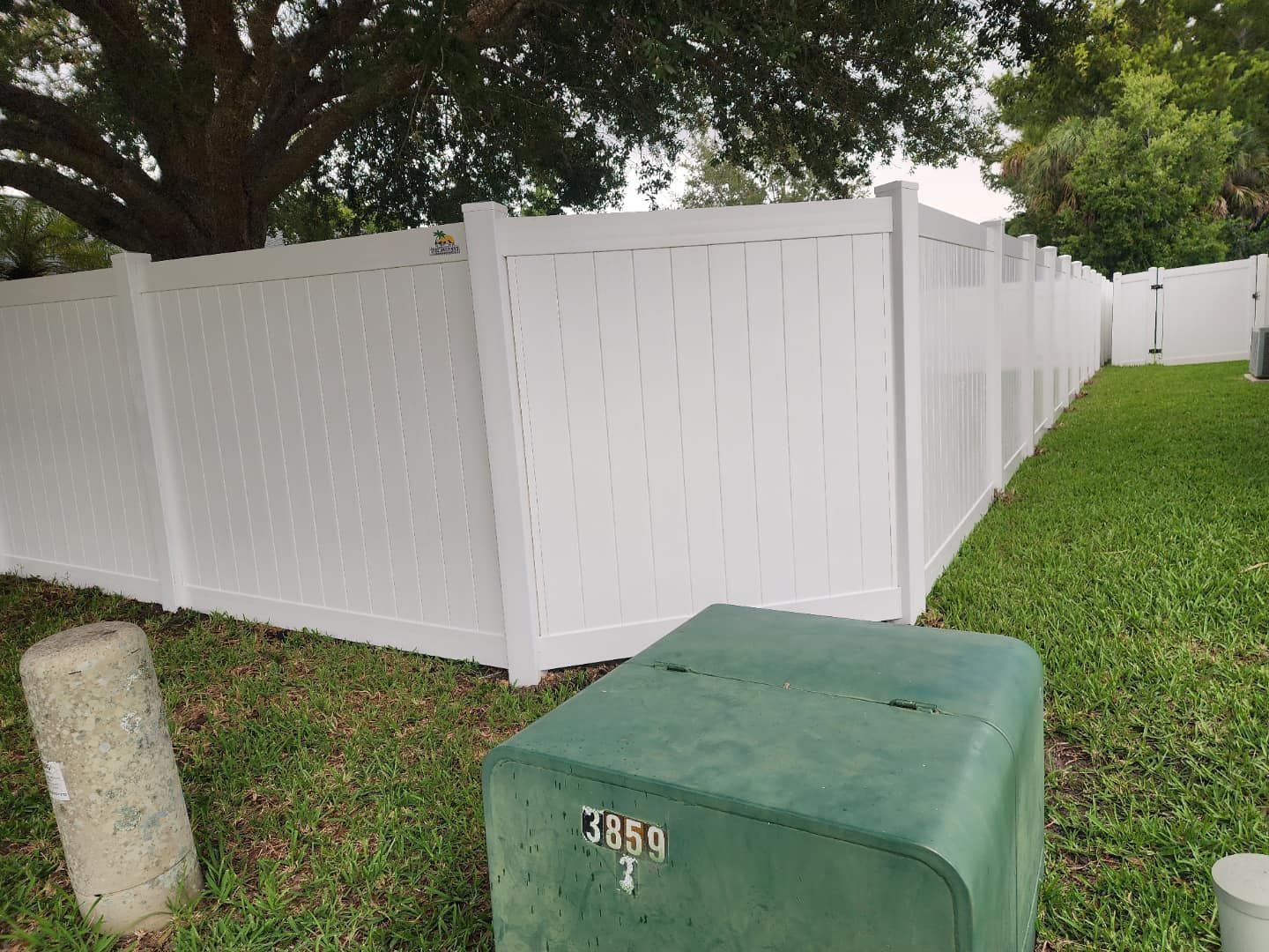 White vinyl fence in a grassy yard, with a green utility box in the foreground.