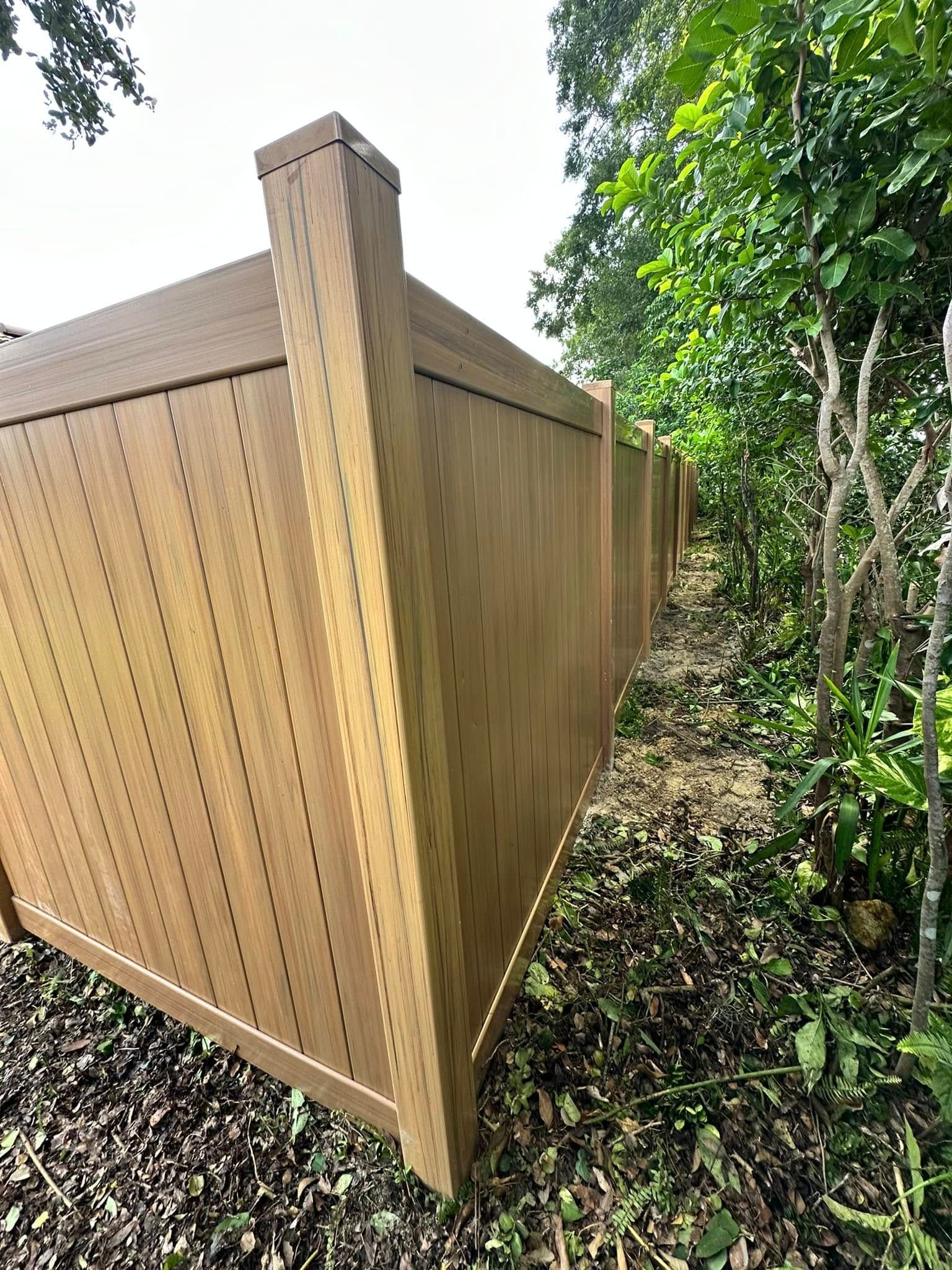 Tan wooden fence in a yard, viewed from a low angle with foliage in the background.