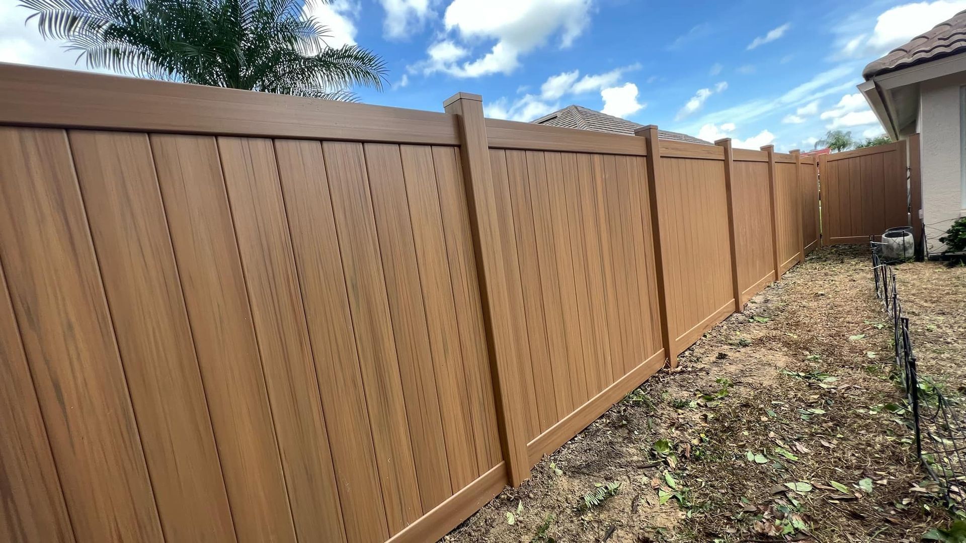 Brown vinyl fence in a yard under a cloudy sky.