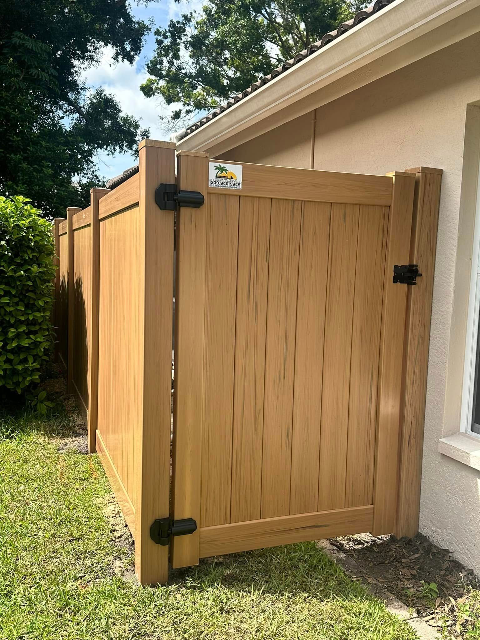 Tan vinyl fence with a gate secured by black hinges and a latch, next to a beige wall.