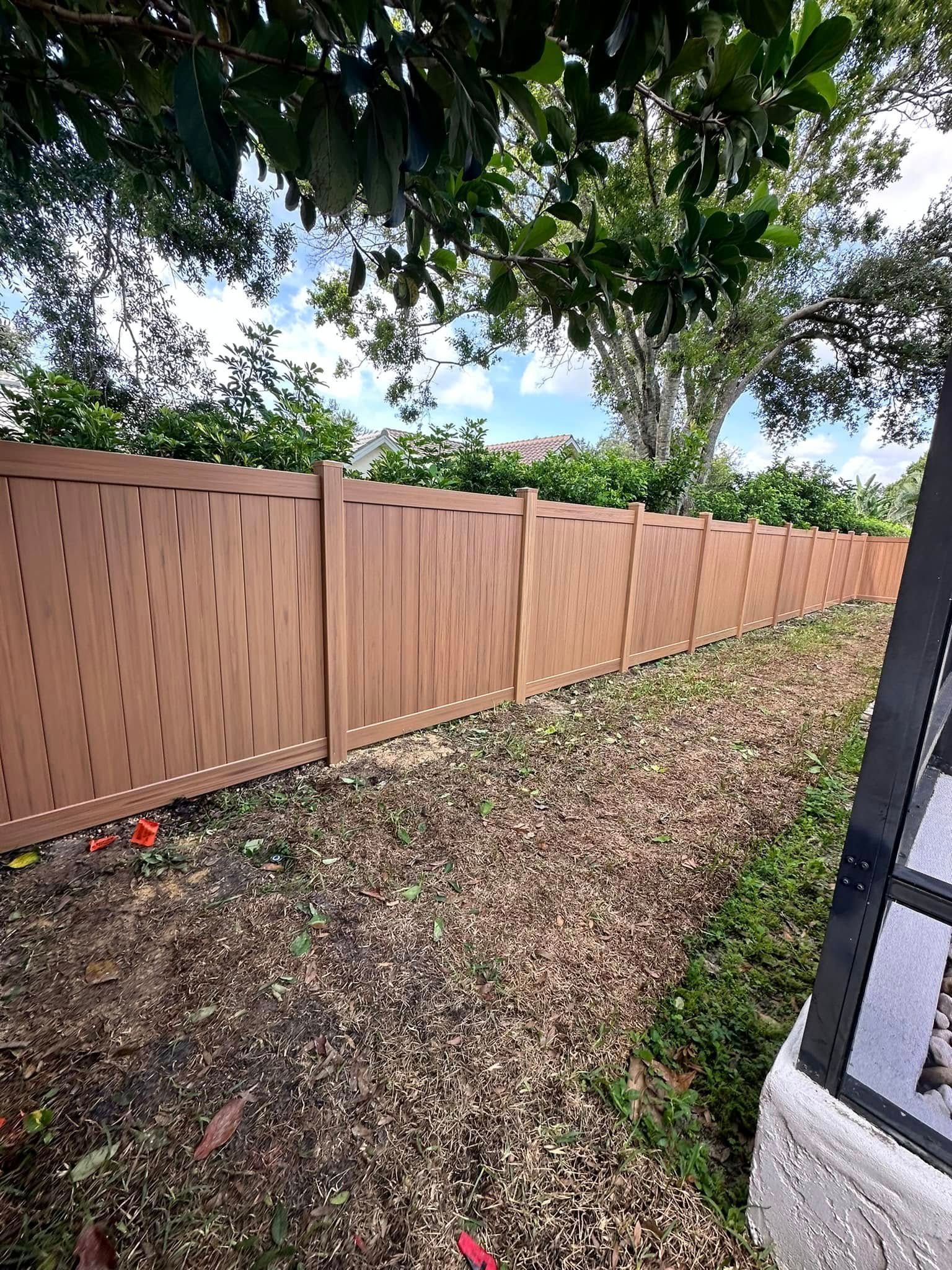 Brown vinyl fence in a yard with foliage and a decorative gate.