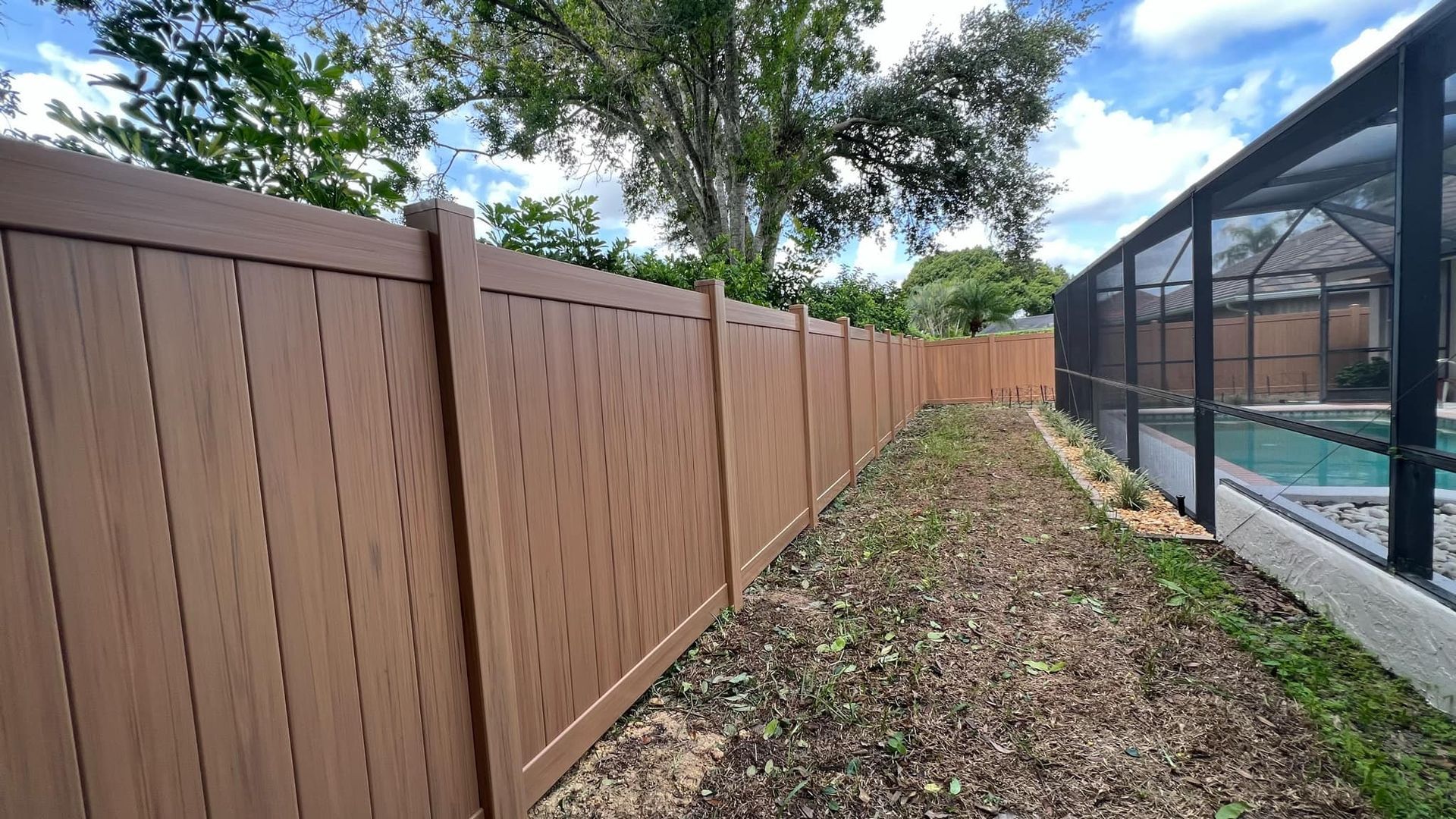 Brown vinyl fence surrounding a yard, next to a screened pool enclosure.