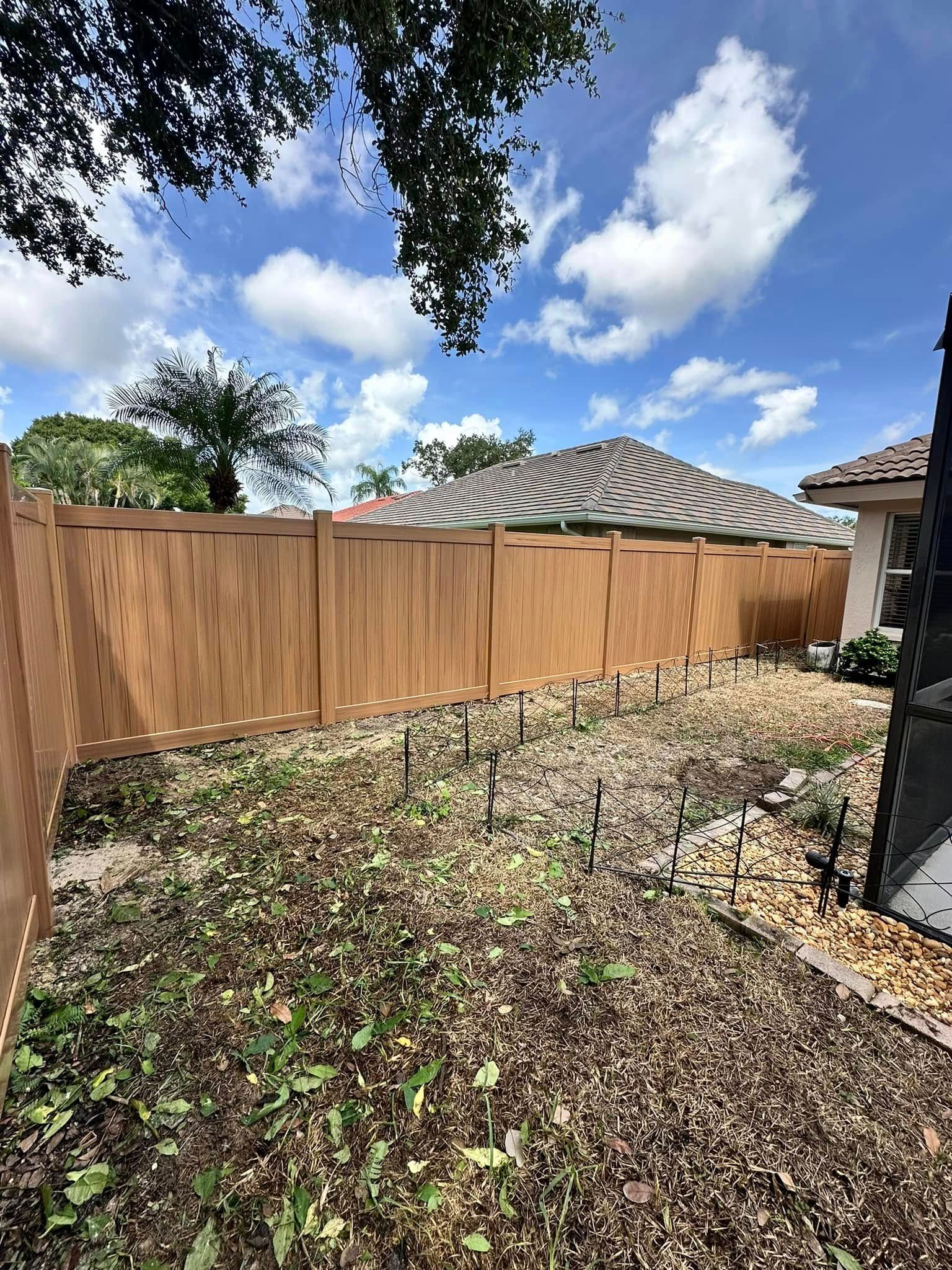 Wooden fence in a yard with sparse vegetation under a bright blue sky with clouds.