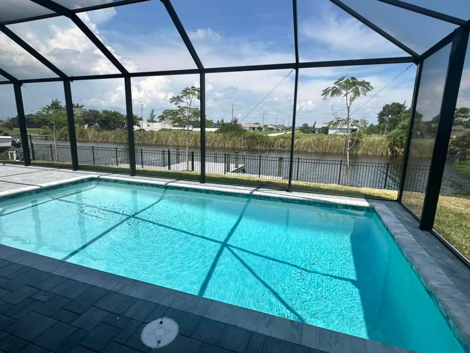 Pool enclosed by a screen, blue water. Black framing, grassy area beyond. Bright sky.