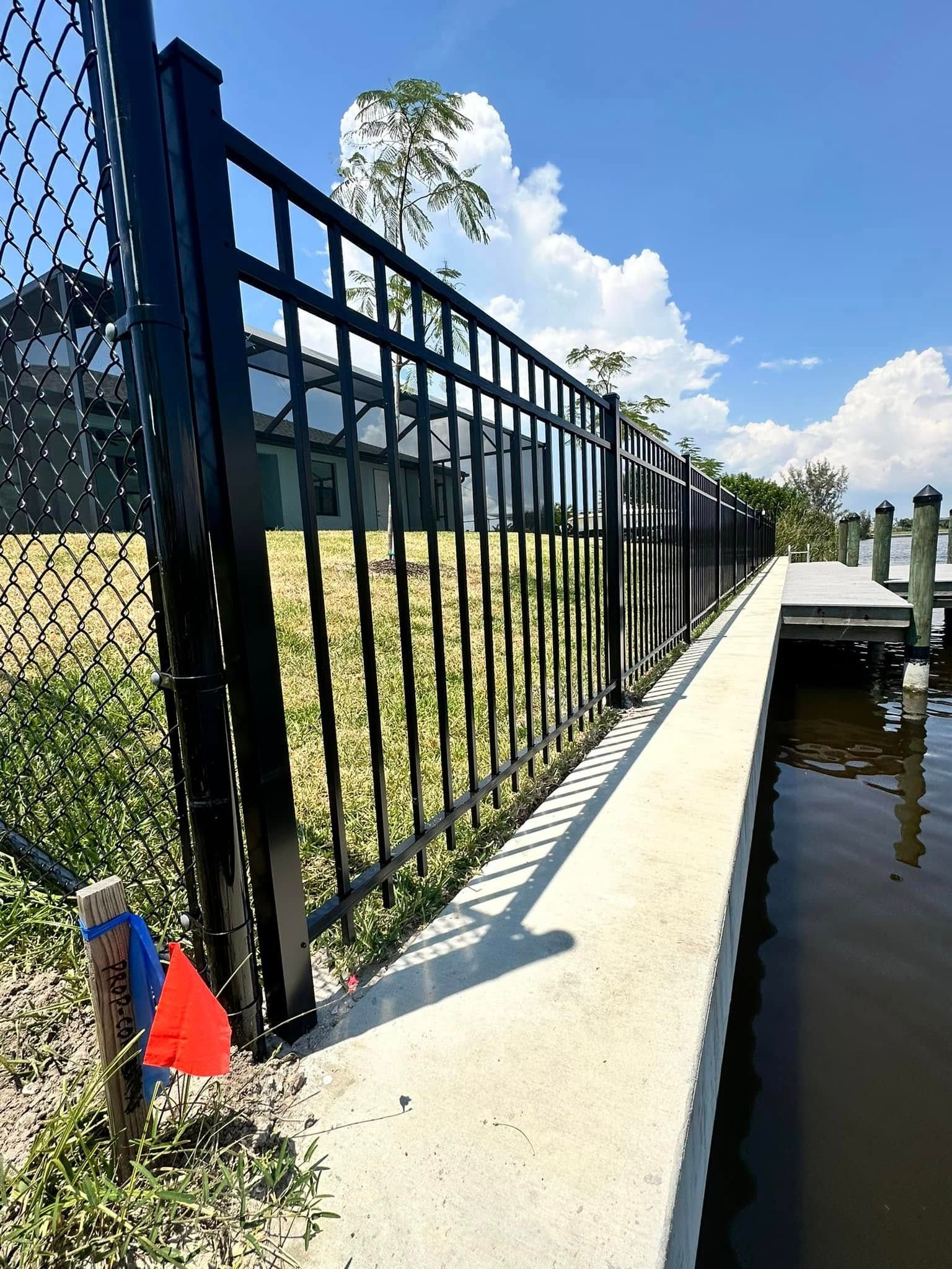 Black metal fence along a concrete dock, next to water on a sunny day.