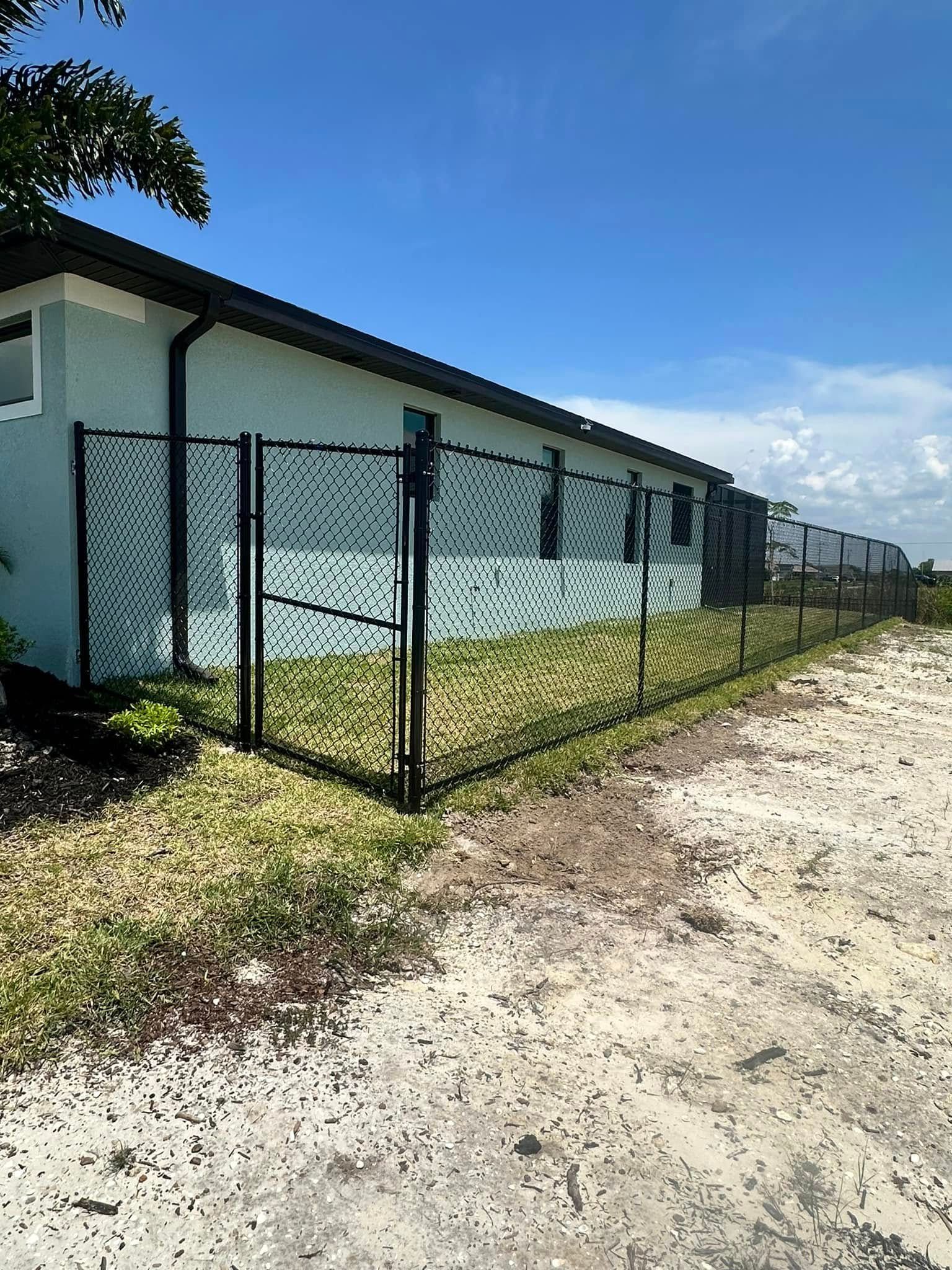 Black chain-link fence surrounds a light blue building under a blue sky.